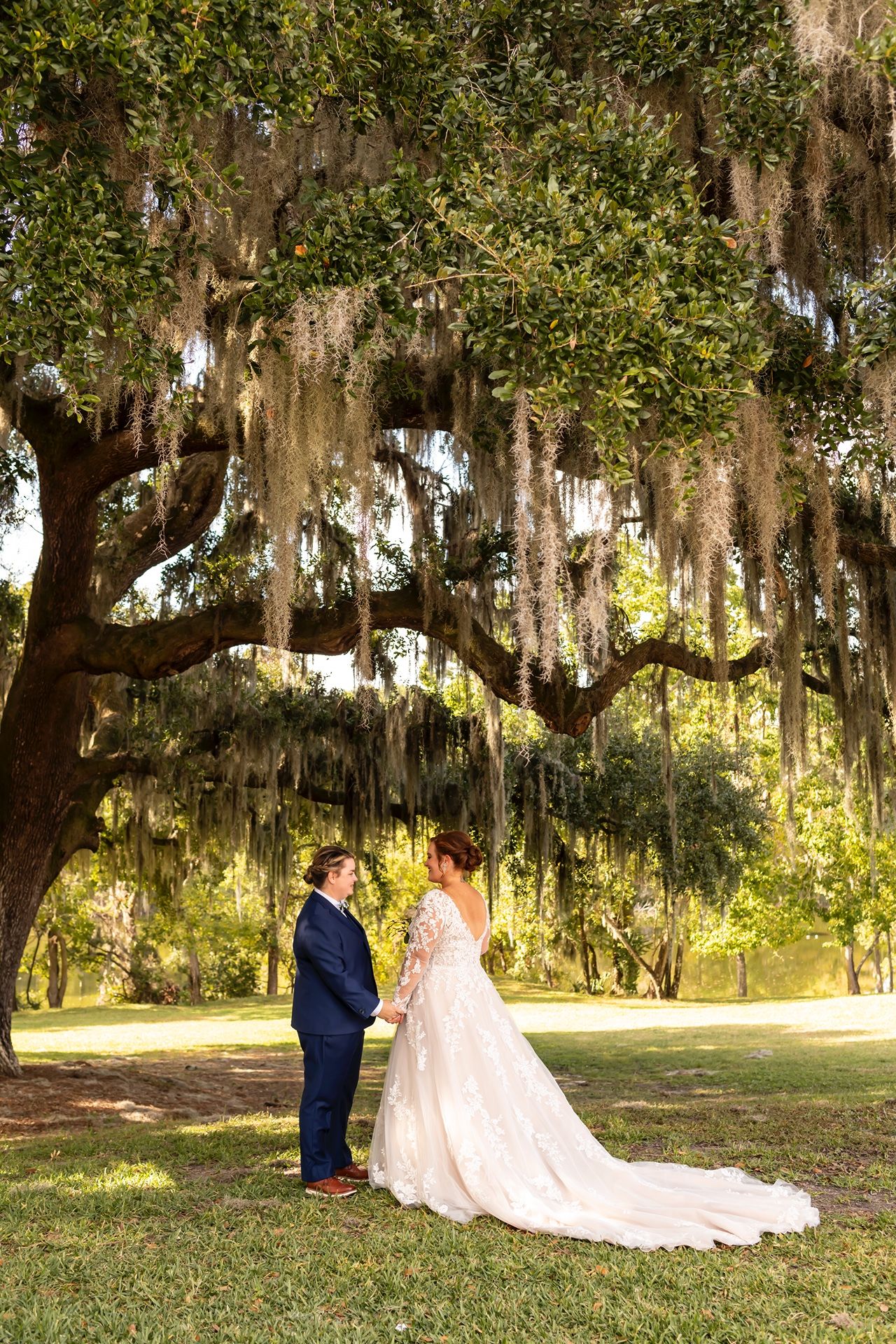 A couple shares a romantic moment under majestic Spanish moss-draped oak trees in an outdoor garden setting.
