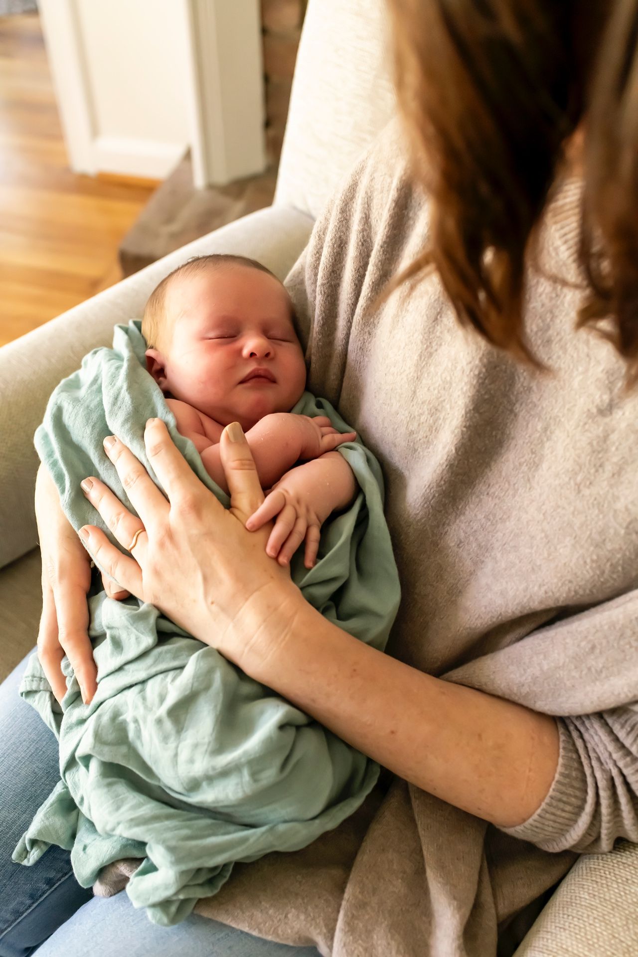 Sleeping newborn baby wrapped in mint green swaddle blanket resting on parent's lap.