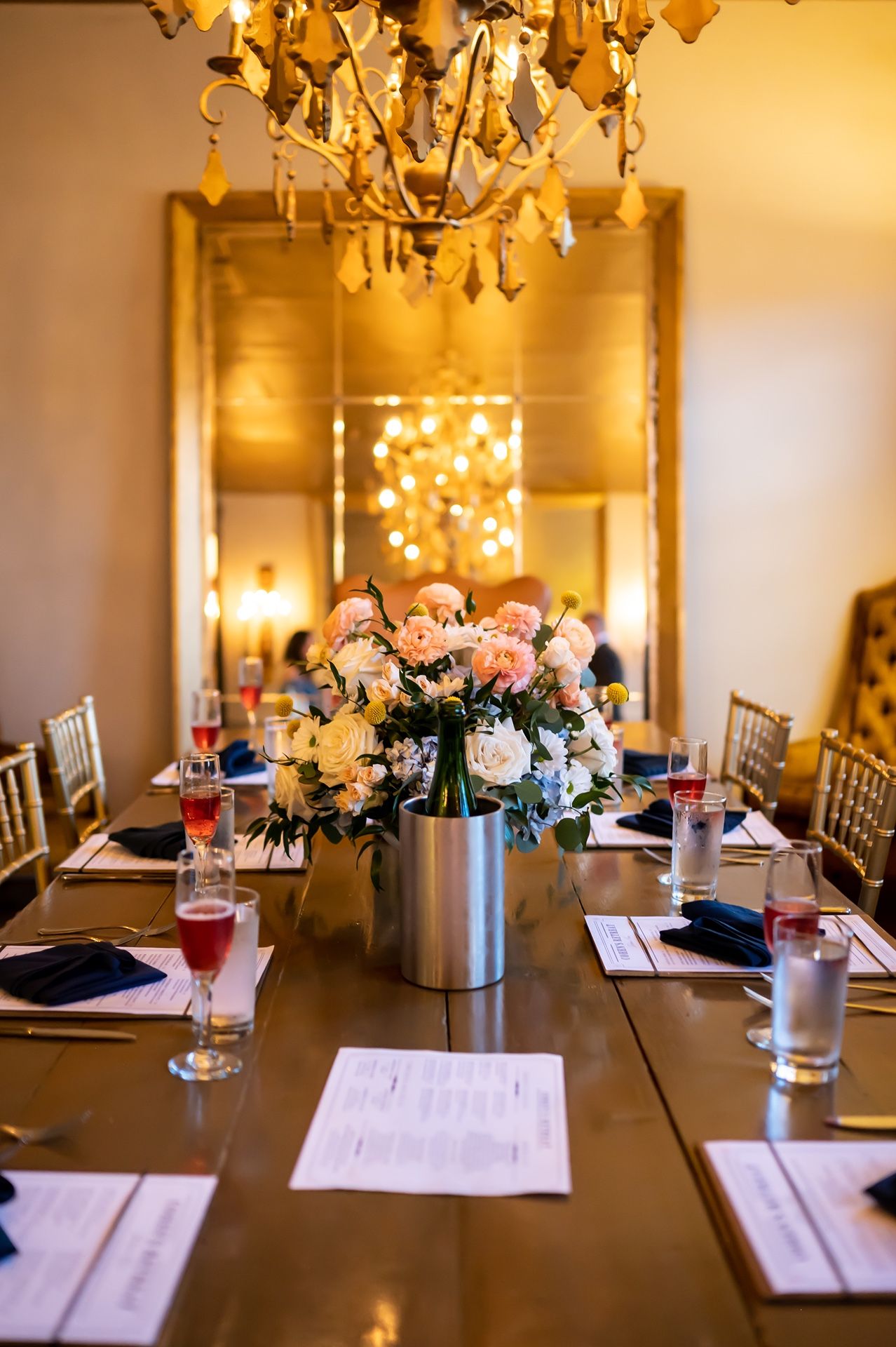 Elegant dining table with floral centerpiece, chandelier, and place settings under warm lighting in a formal event space.