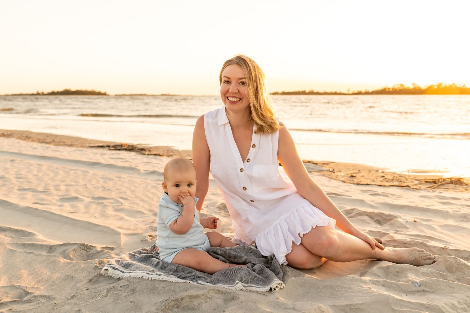 Parent and child playing together on sandy beach at sunset during golden hour as waves roll in along shoreline.
