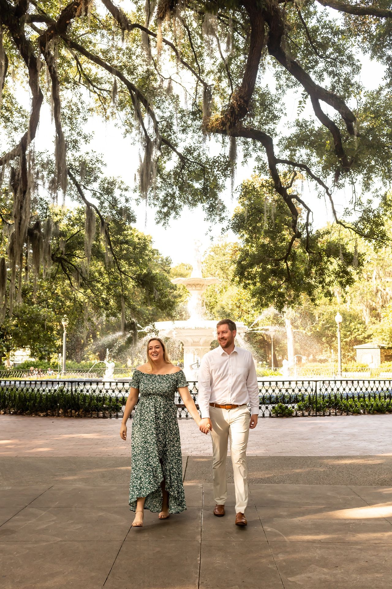A couple walks together on a path under Spanish moss draped oak trees in a romantic Southern garden setting.