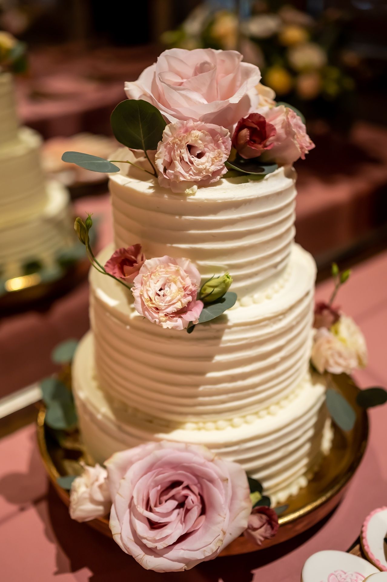 Three-tiered white wedding cake decorated with delicate pink roses and greenery on display.