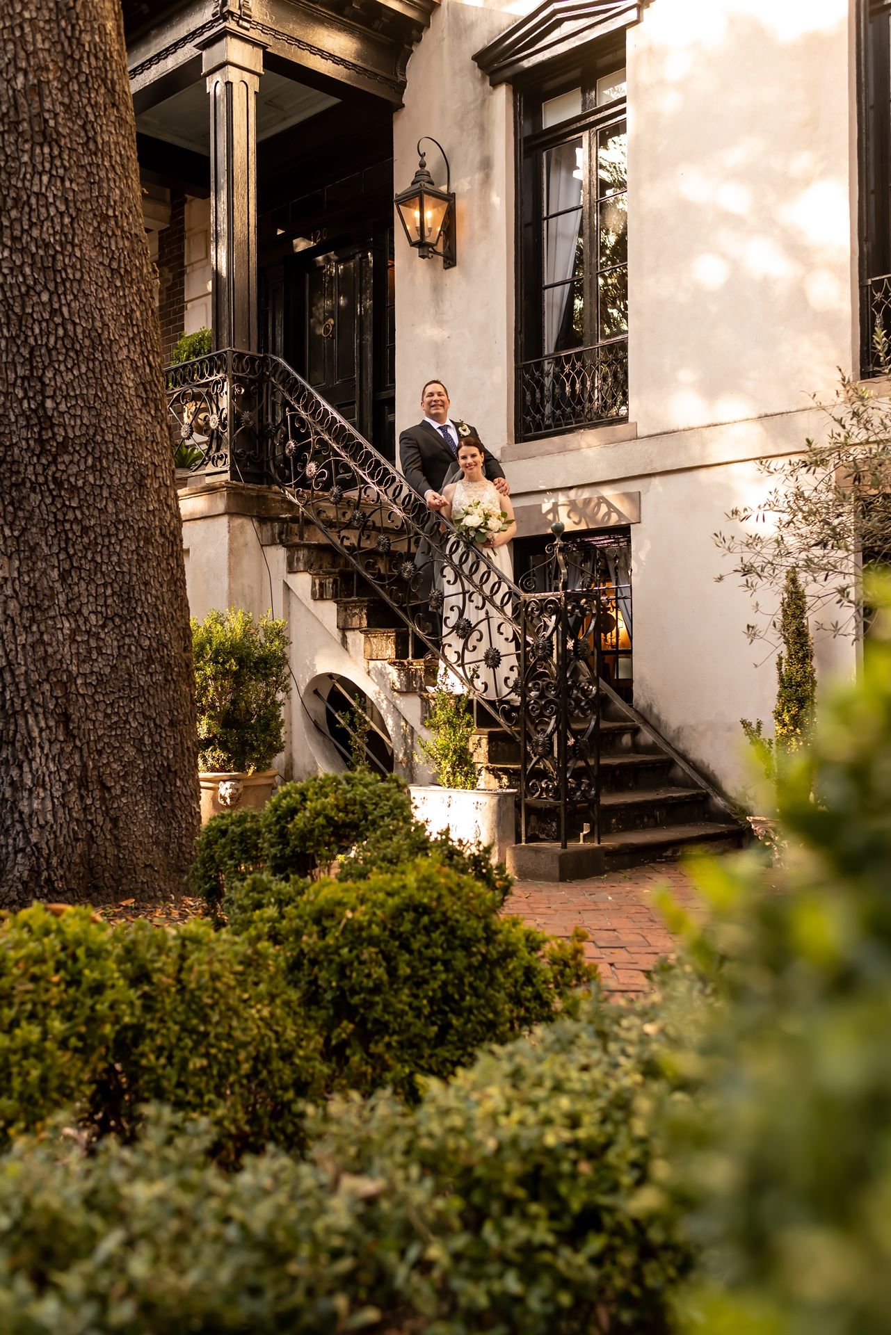 Elegant staircase entrance to historic townhouse with ornate iron railings and lush garden landscaping at dusk.