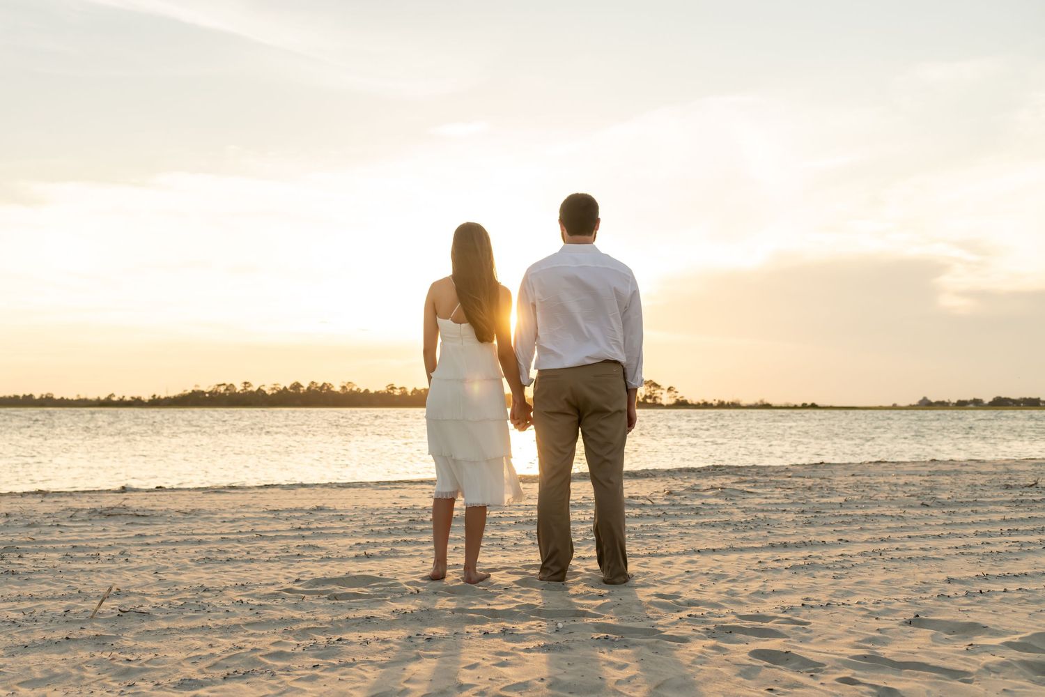 A couple walking hand in hand along a pristine white sandy beach at sunset by the ocean.