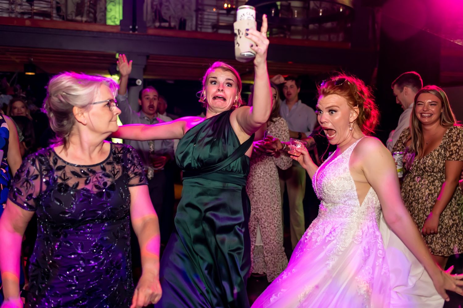 People dancing and enjoying themselves at a vibrant nightclub with pink and purple lighting.