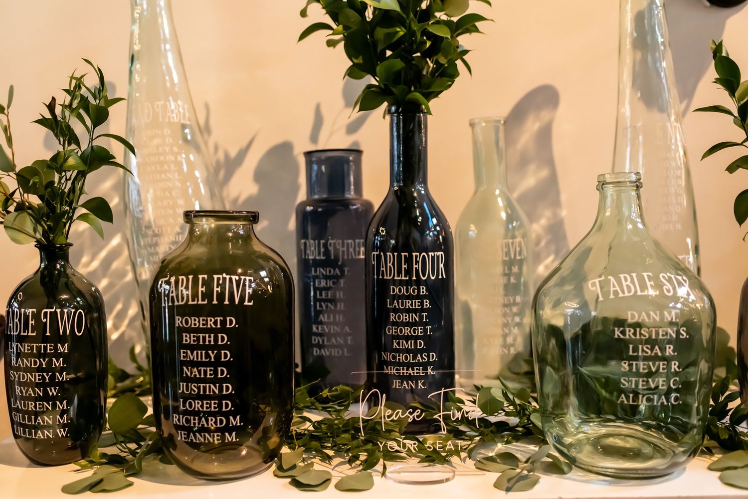 Clear glass bottles labeled with different essential oils displayed in a row with green plant leaves and herbs inside them.