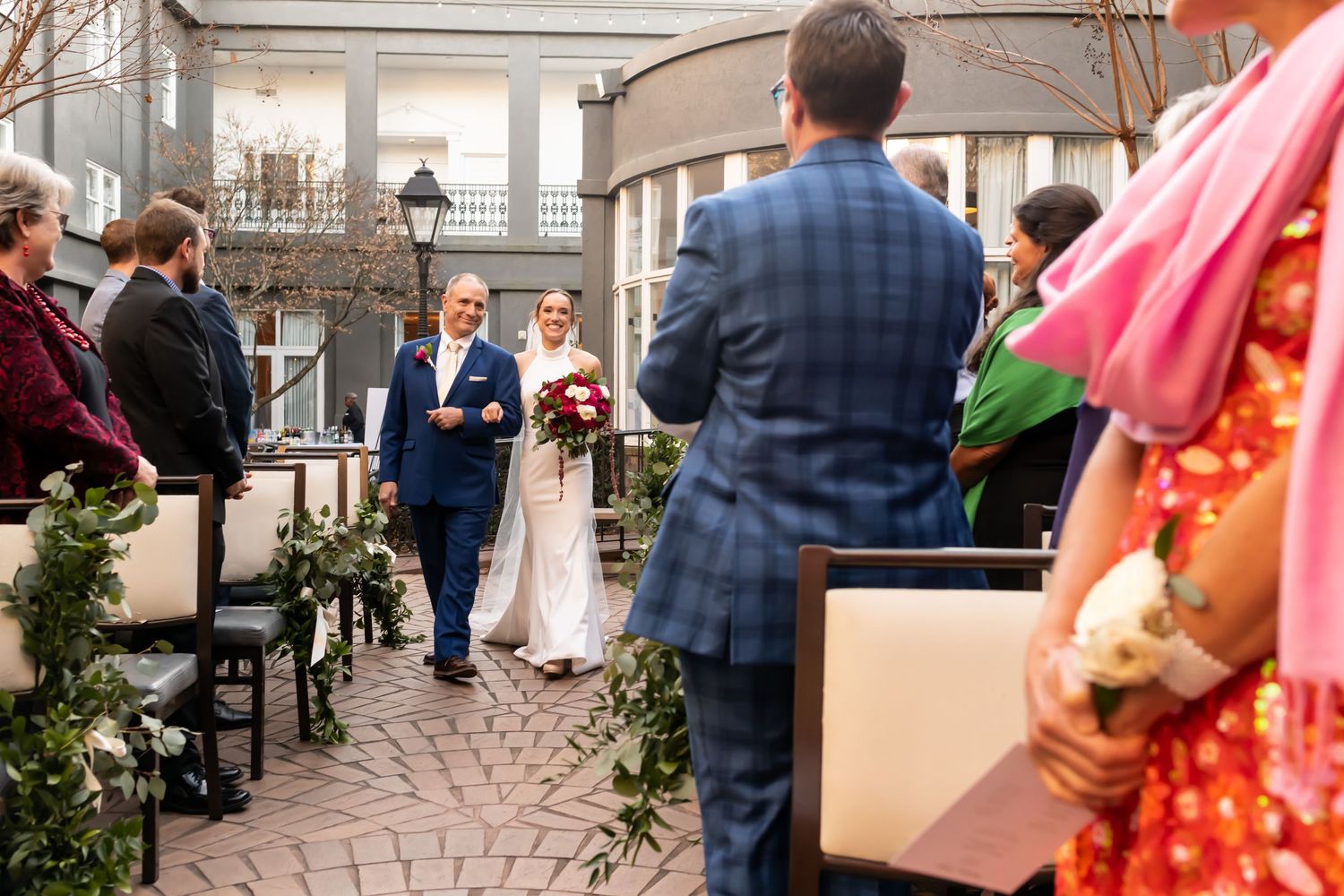 A waterfront wedding ceremony with guests seated along a marina dock under strings of cafe lights at sunset.