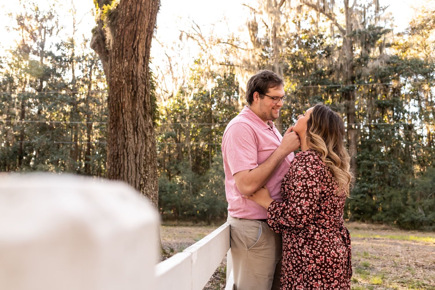 A couple embraces tenderly in a golden-lit wooded area during an outdoor portrait session.