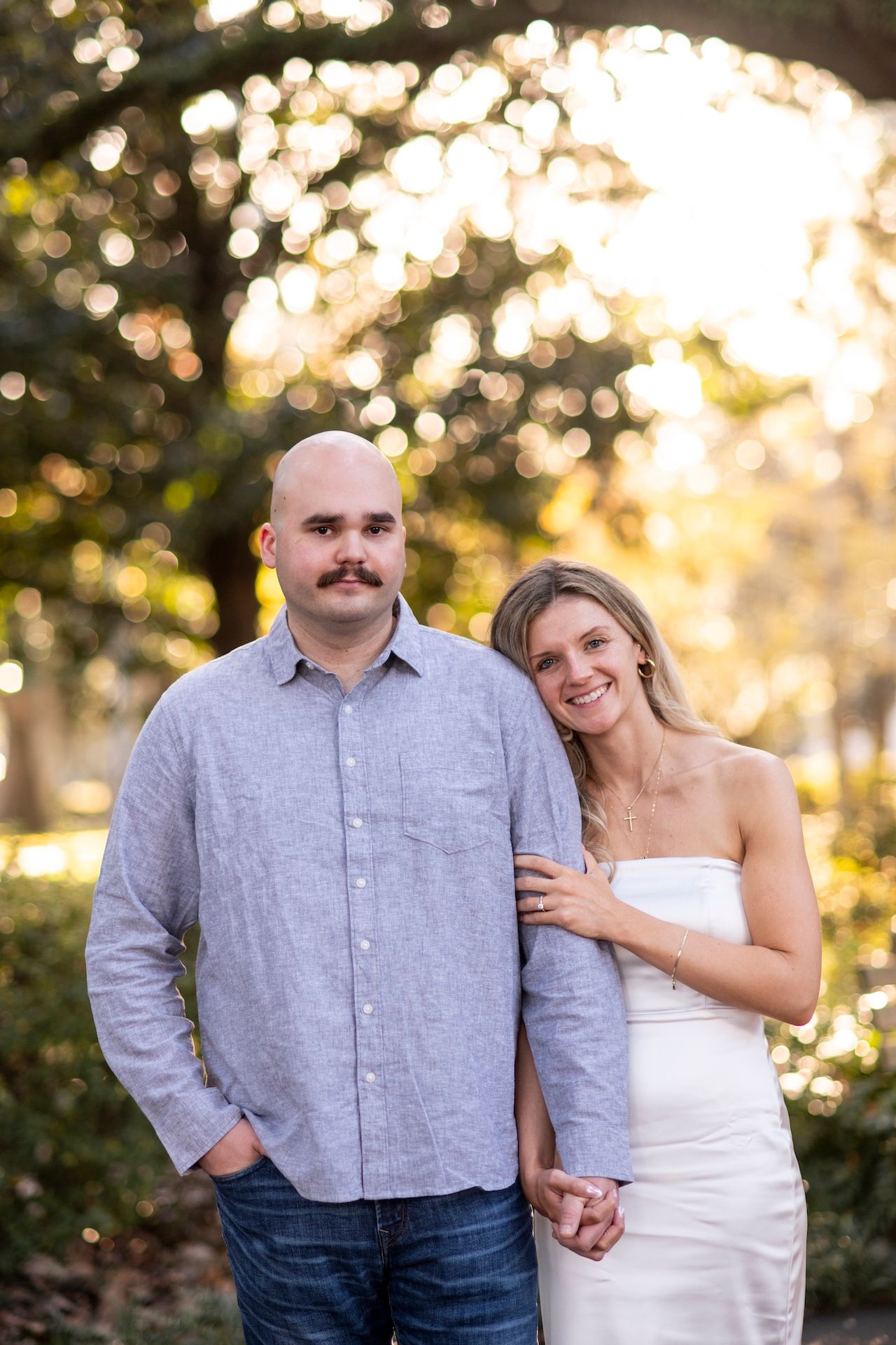 A couple poses together at Forsyth Park during golden hour with bokeh lighting effects in the background.