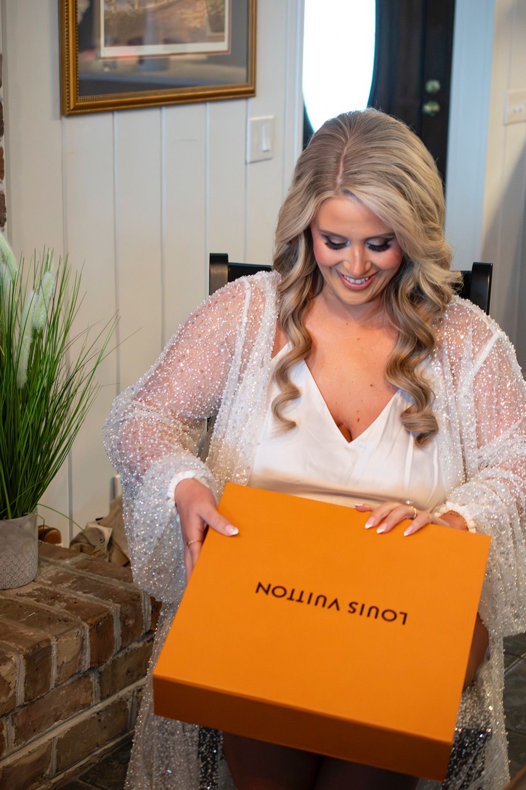 A person in a sparkly dress excitedly opens an orange Louis Vuitton shopping box.
