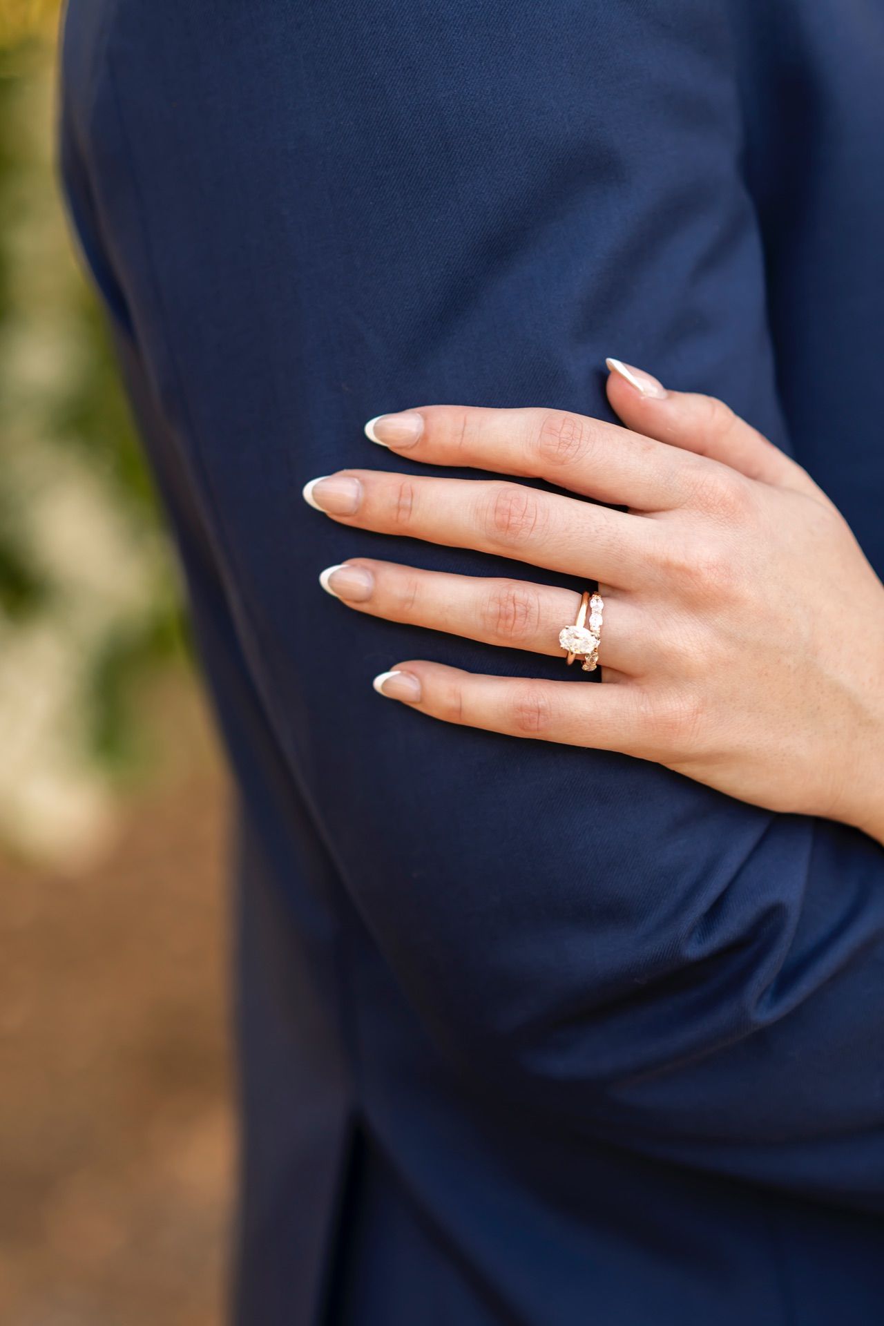 Close-up view of hands wearing gold engagement rings against a navy blue background.