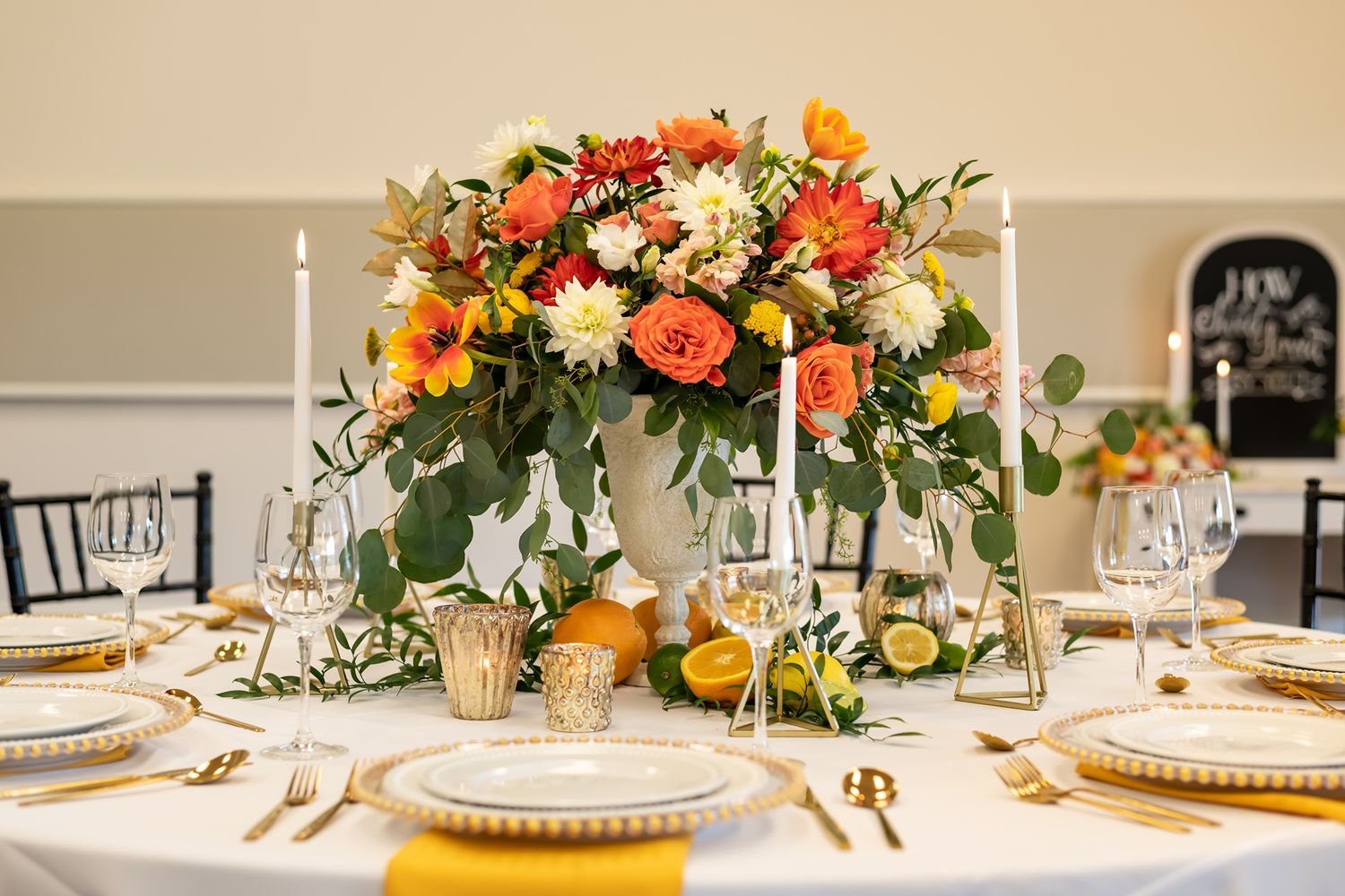 Elegant wedding table setting with coral and orange floral centerpiece, gold chargers, and white candlesticks.