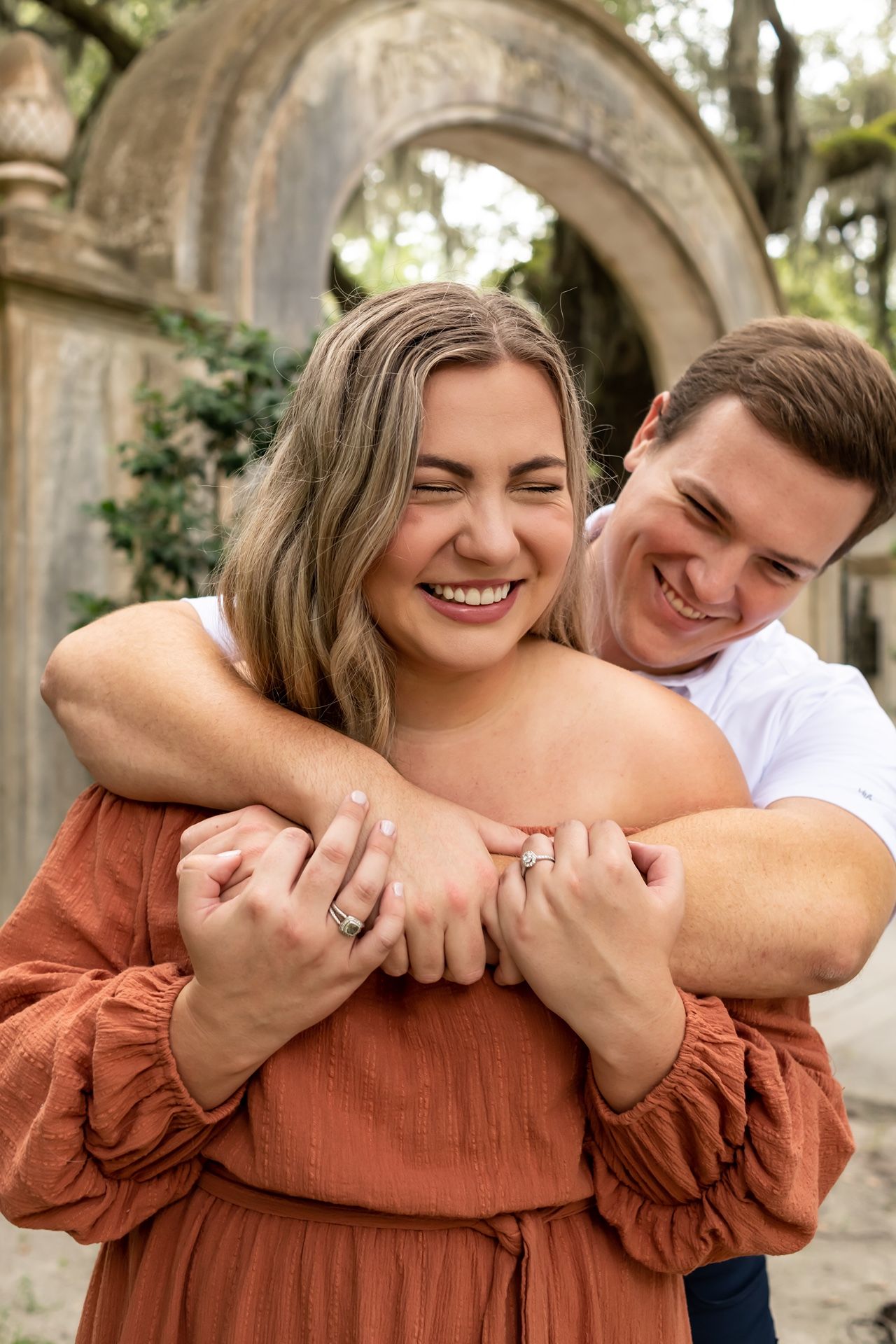 A joyful couple embraces and laughs together in front of stone archways during an outdoor photo session.