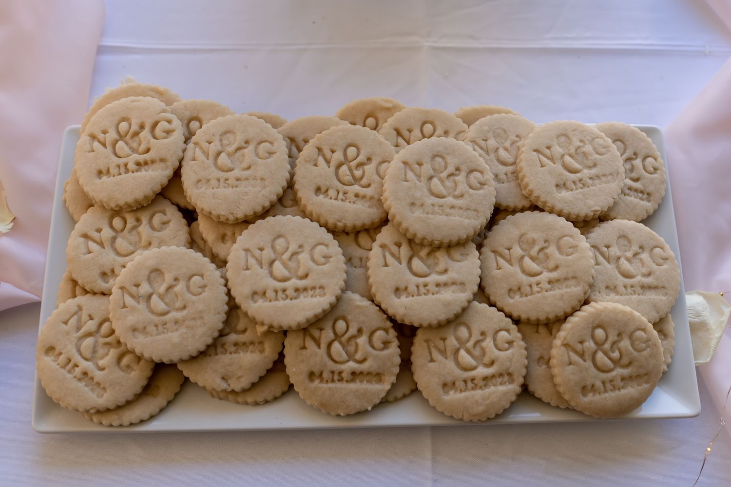 A plate of light-colored sandwich cookies with embossed designs arranged neatly in rows.