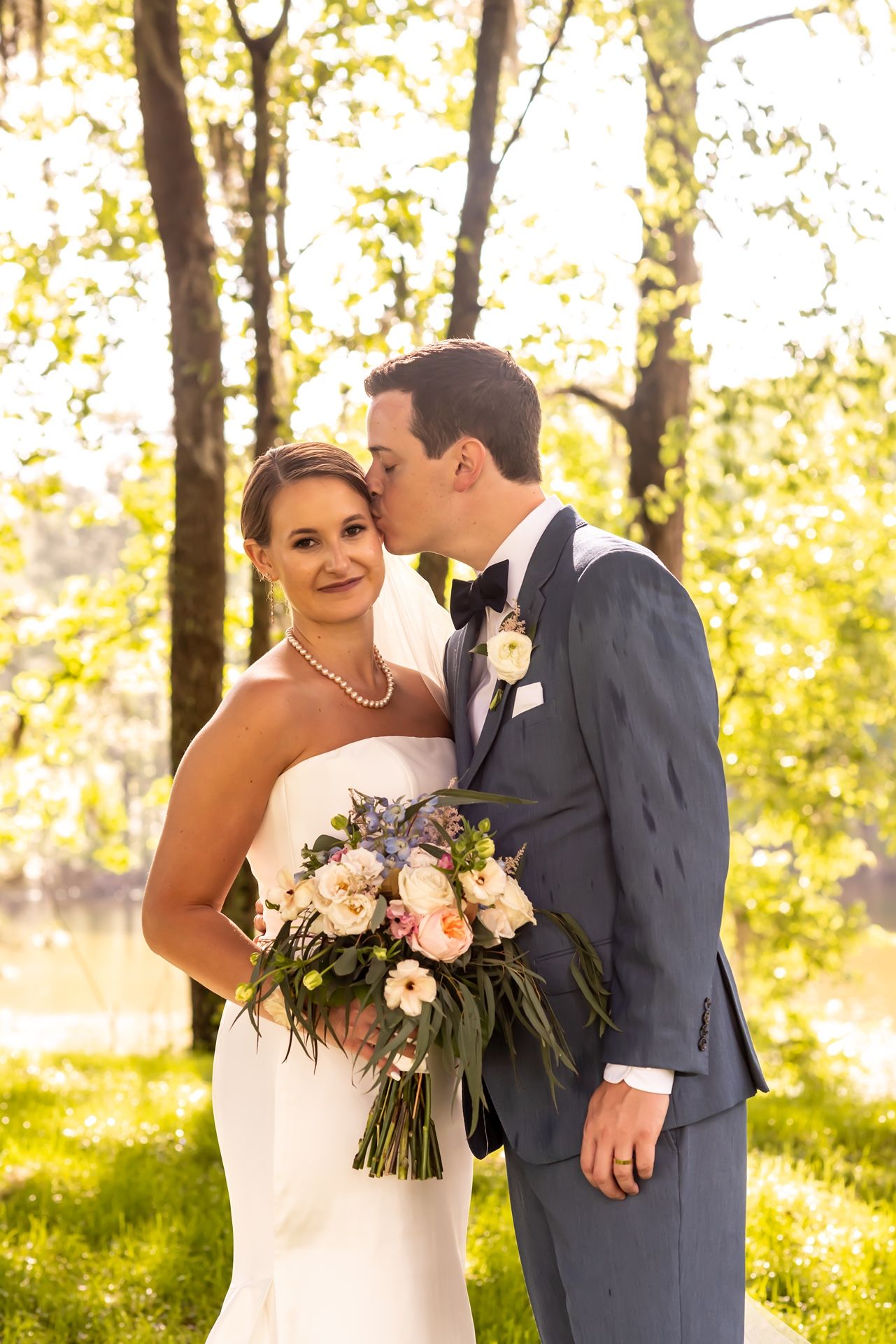 A romantic wedding moment captured in a sunlit forest with golden autumn foliage glowing in the background.