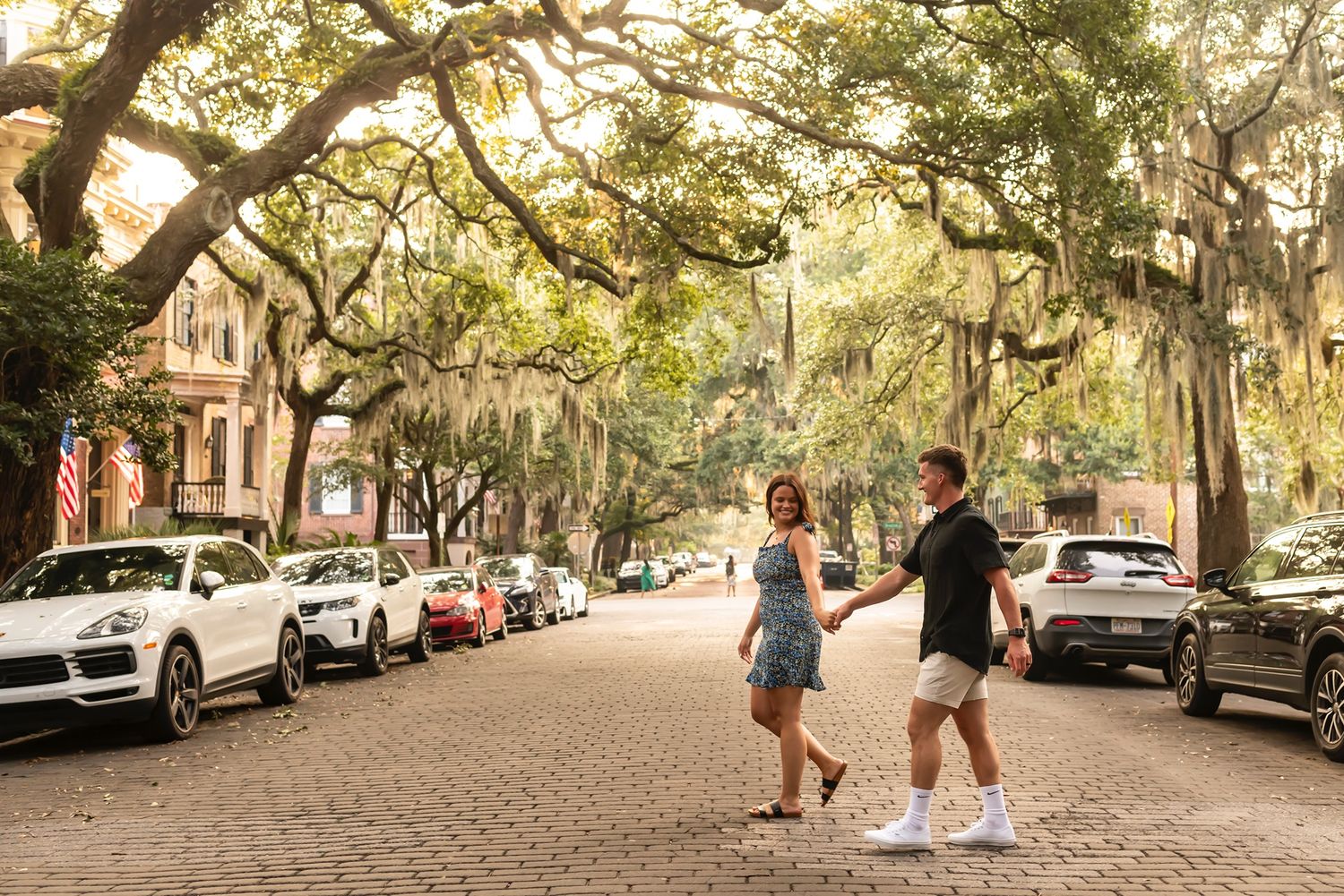 Scenic oak tree-lined street in Savannah with Spanish moss draping over the road and parked cars along the curb.
