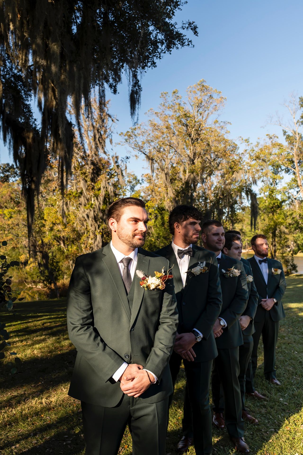 A series of candid photos shows a wedding party in dark suits standing together on a scenic lawn with Spanish moss trees.
