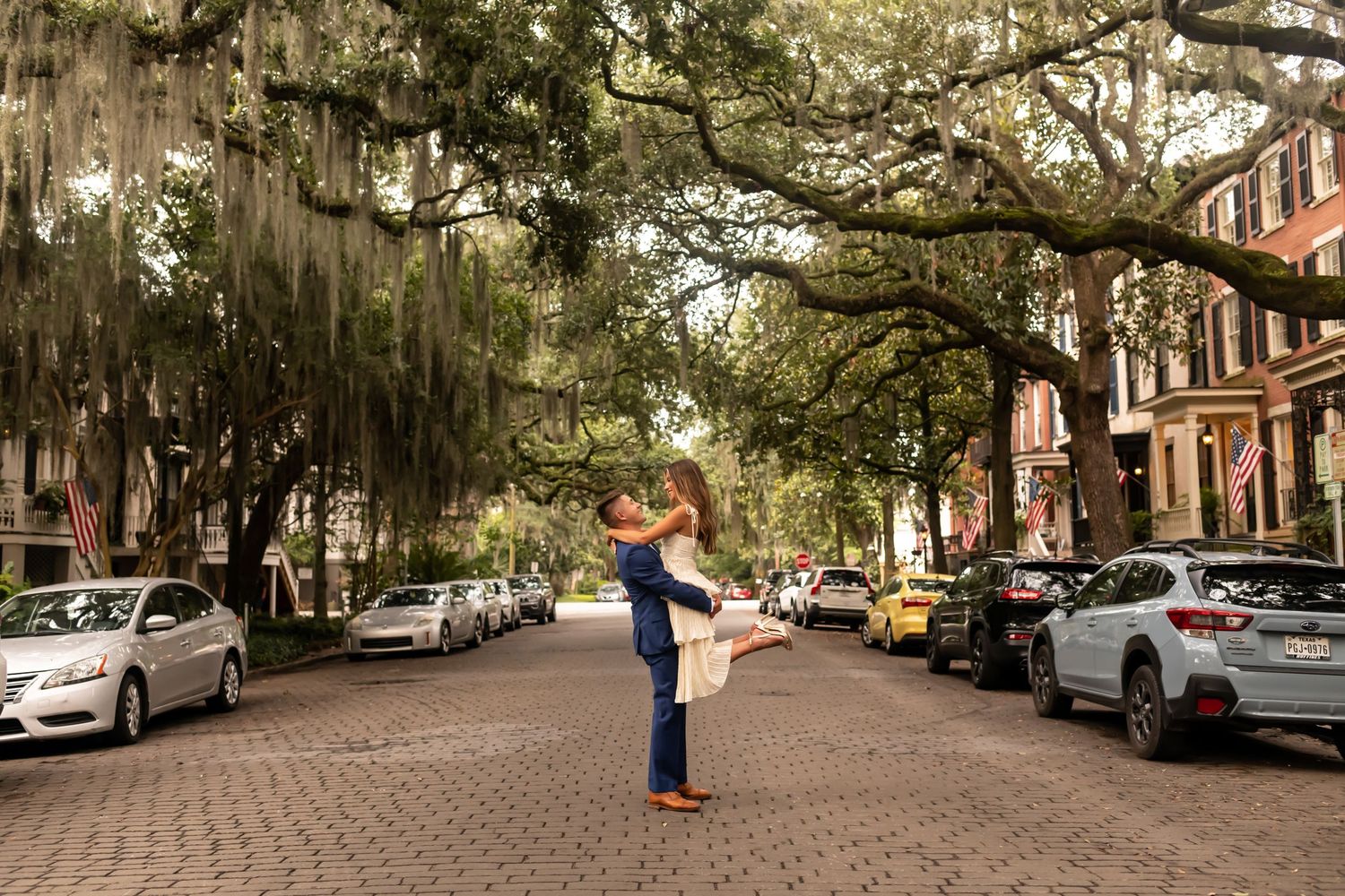 Tree-lined historic cobblestone street in Savannah with Spanish moss draping over parked cars.