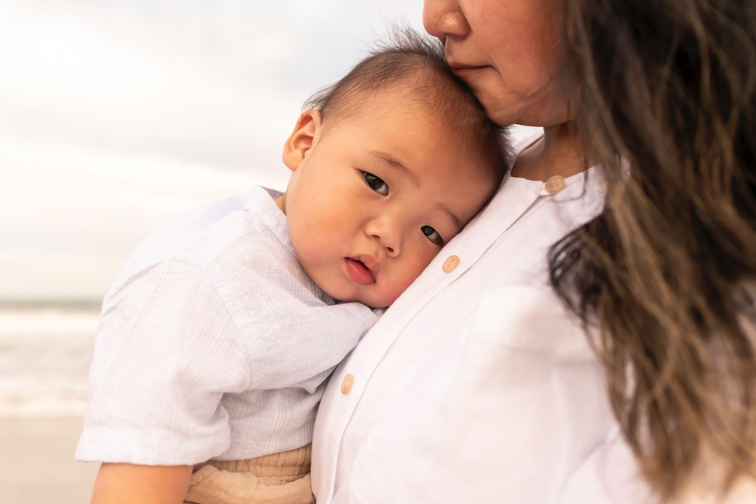 Parent and child share a tender moment in white clothing while relaxing at home.