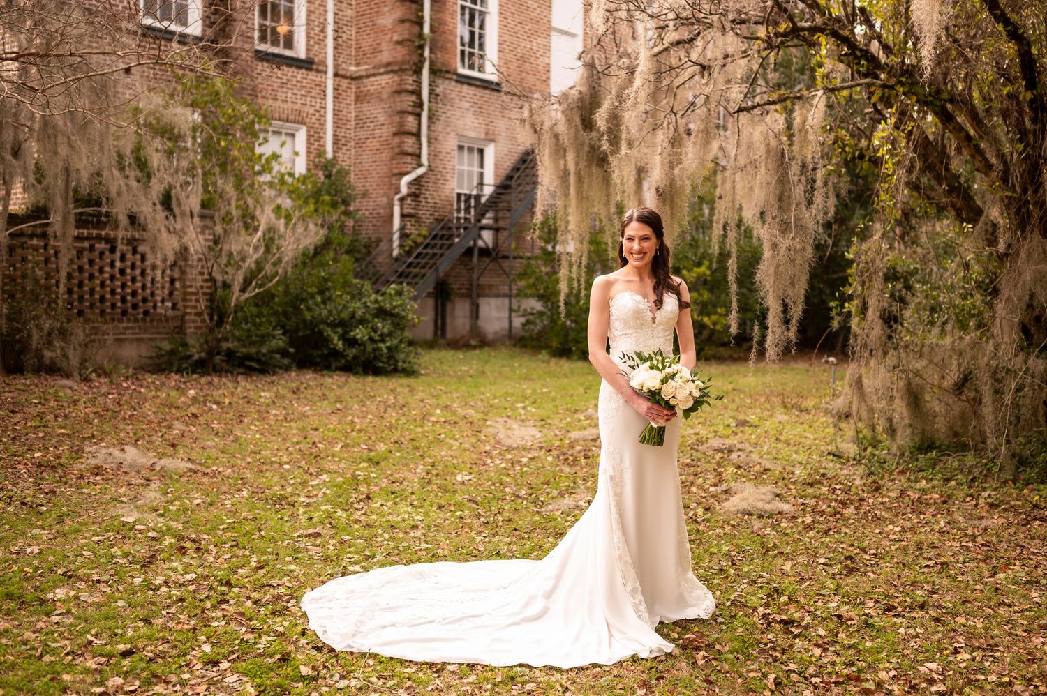 A stunning outdoor bridal portrait in front of a historic brick building with Spanish moss draped trees in the background.