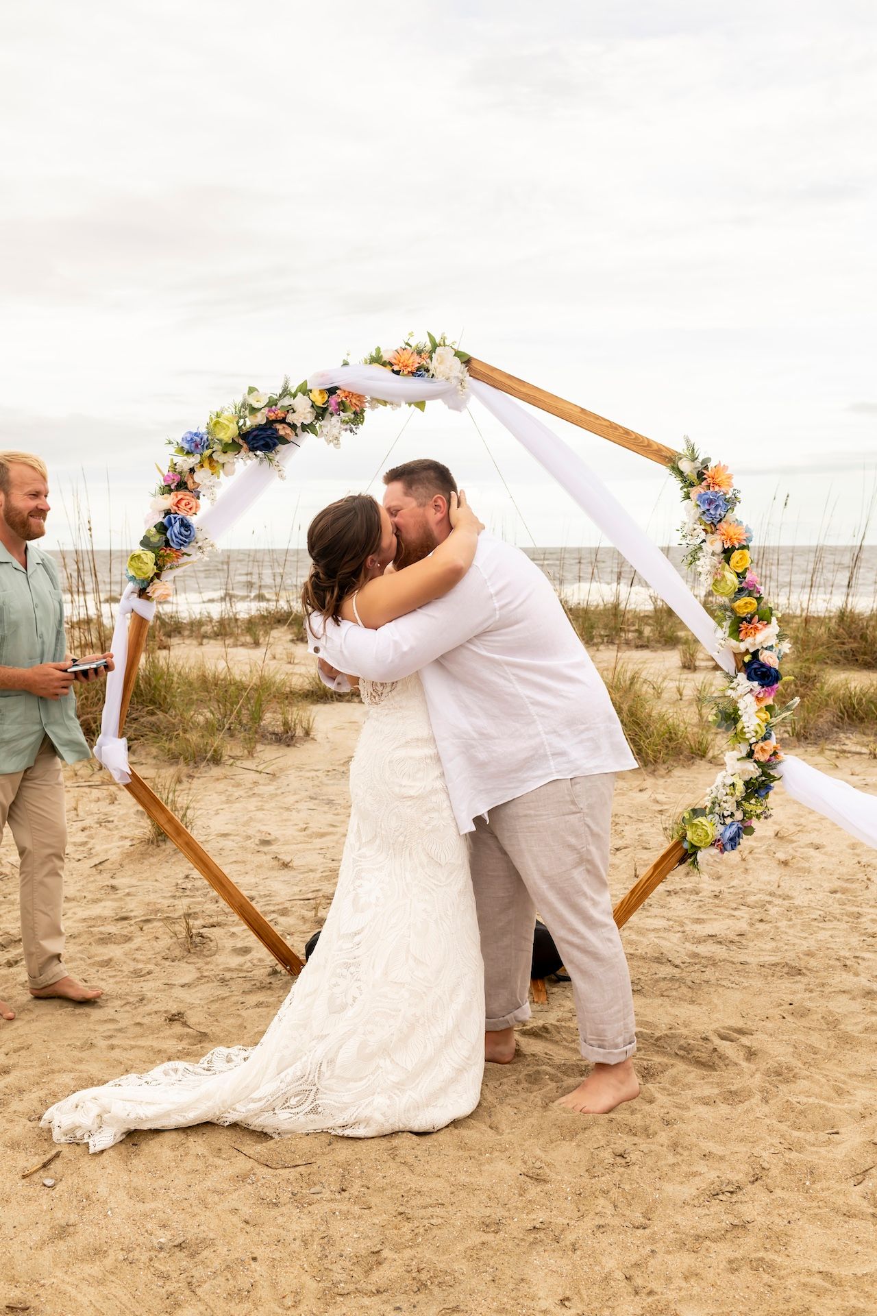 Beach wedding ceremony sequence showing intimate moments under a floral arch decorated with wildflowers and white fabric.