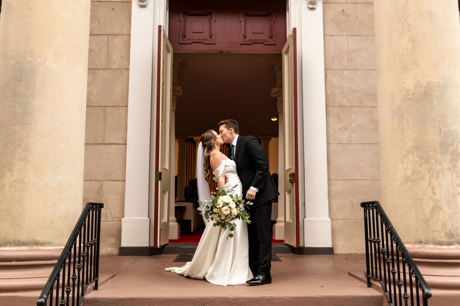 Bride and Groom shares a romantic moment in front of a grand entrance with stone columns and railings at a church in Savannah, Georgia.