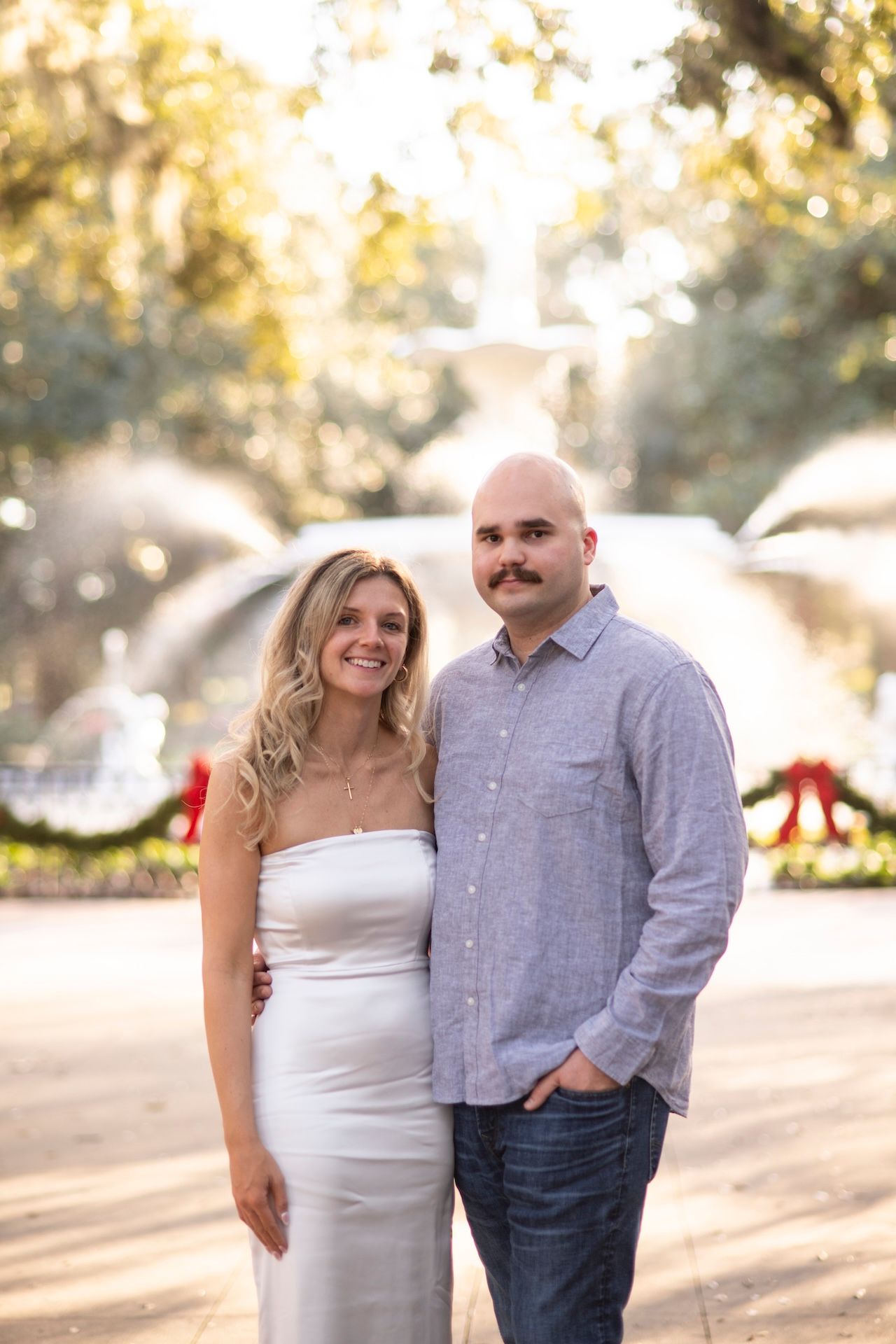 A couple poses together outdoors, with the person in a white dress on the left and a casual button-down shirt on the right.