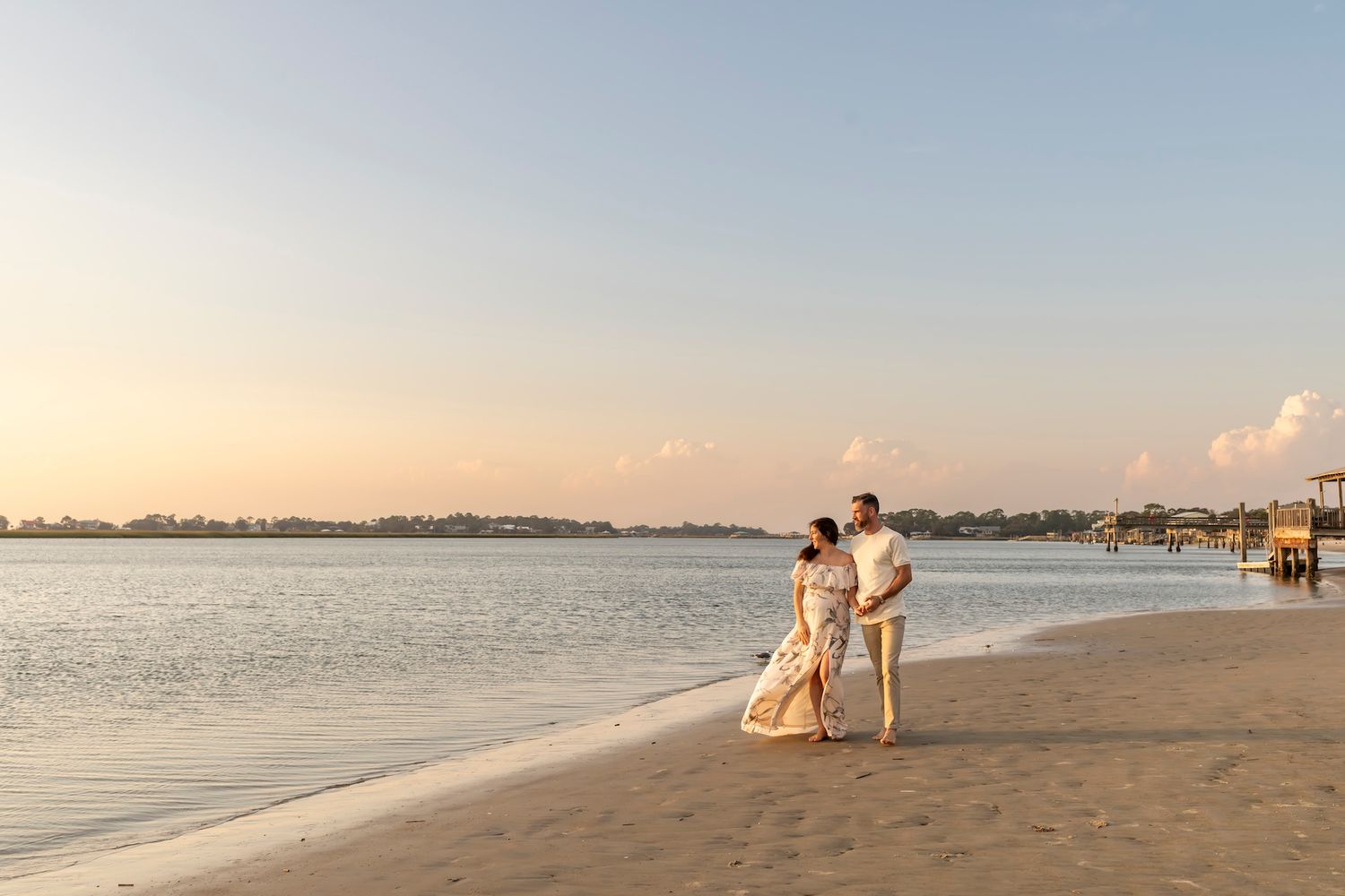 Tranquil beachfront panorama at sunset with people strolling along sandy shore as gentle waves meet the coastline.