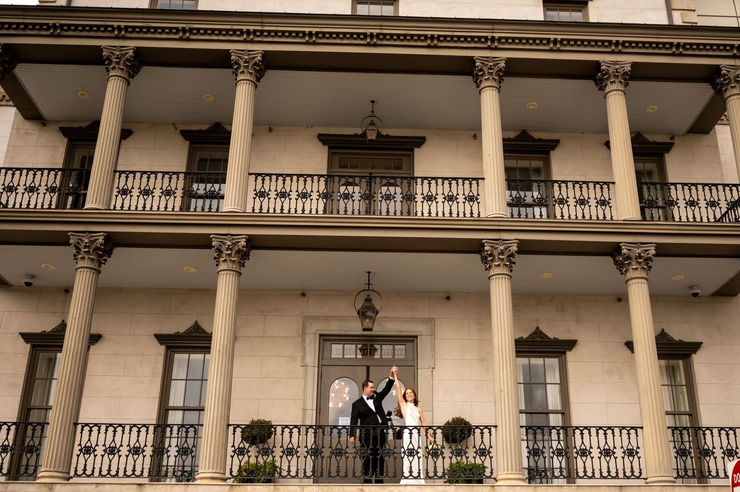 A bride and groom in Savannah, Georgia since with a historic cream-colored building with classical columns and balconies.