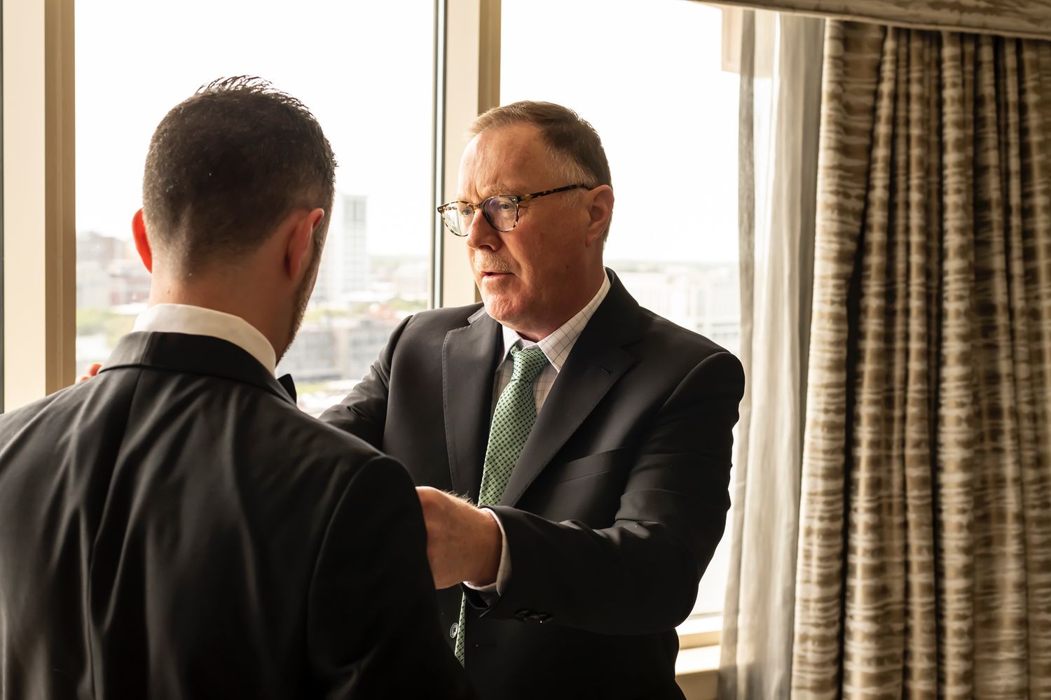 Two businessmen in suits having a professional conversation by a window with natural lighting.