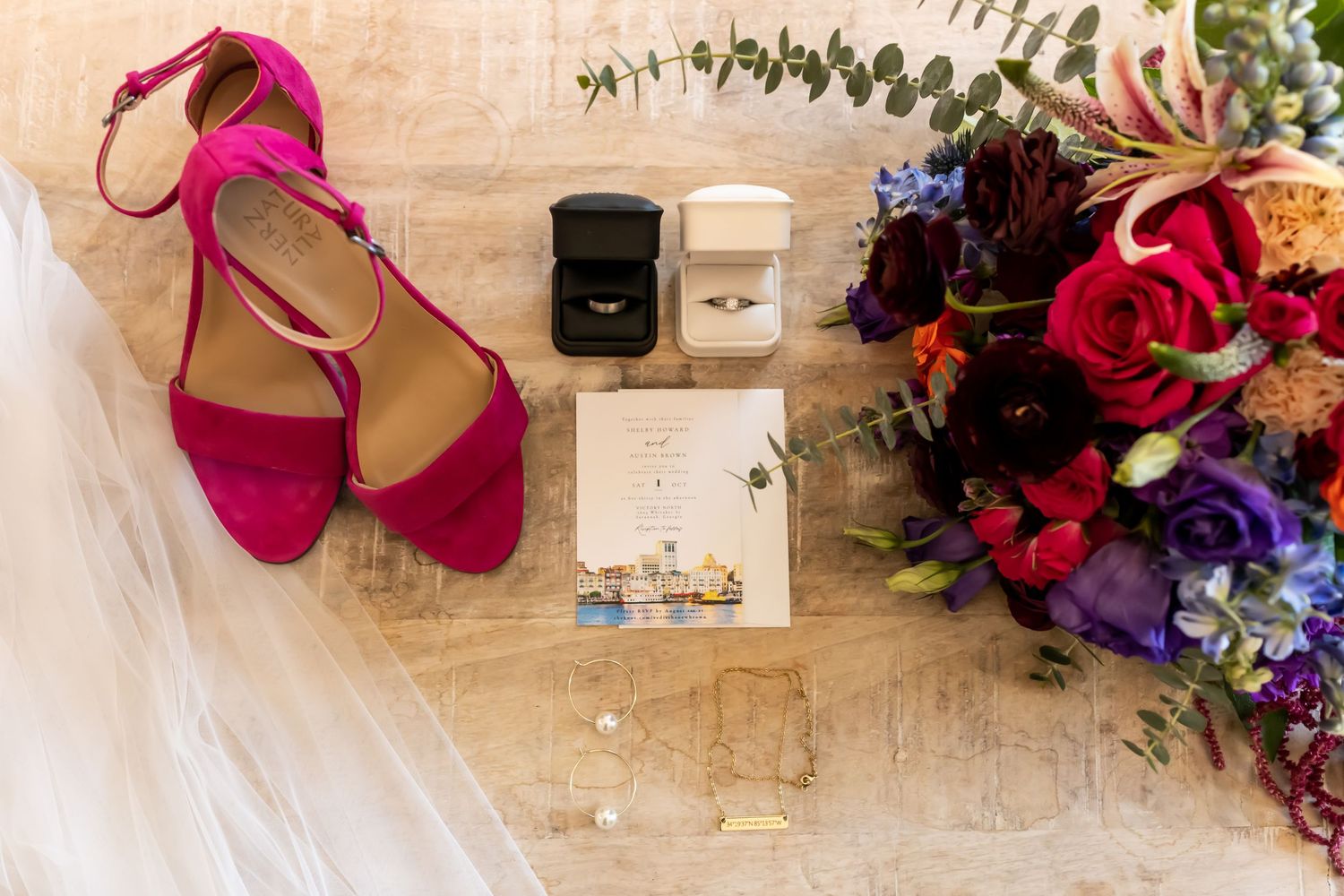 Wedding accessories including pink shoes, floral bouquet, and jewelry arranged on light wooden surface.