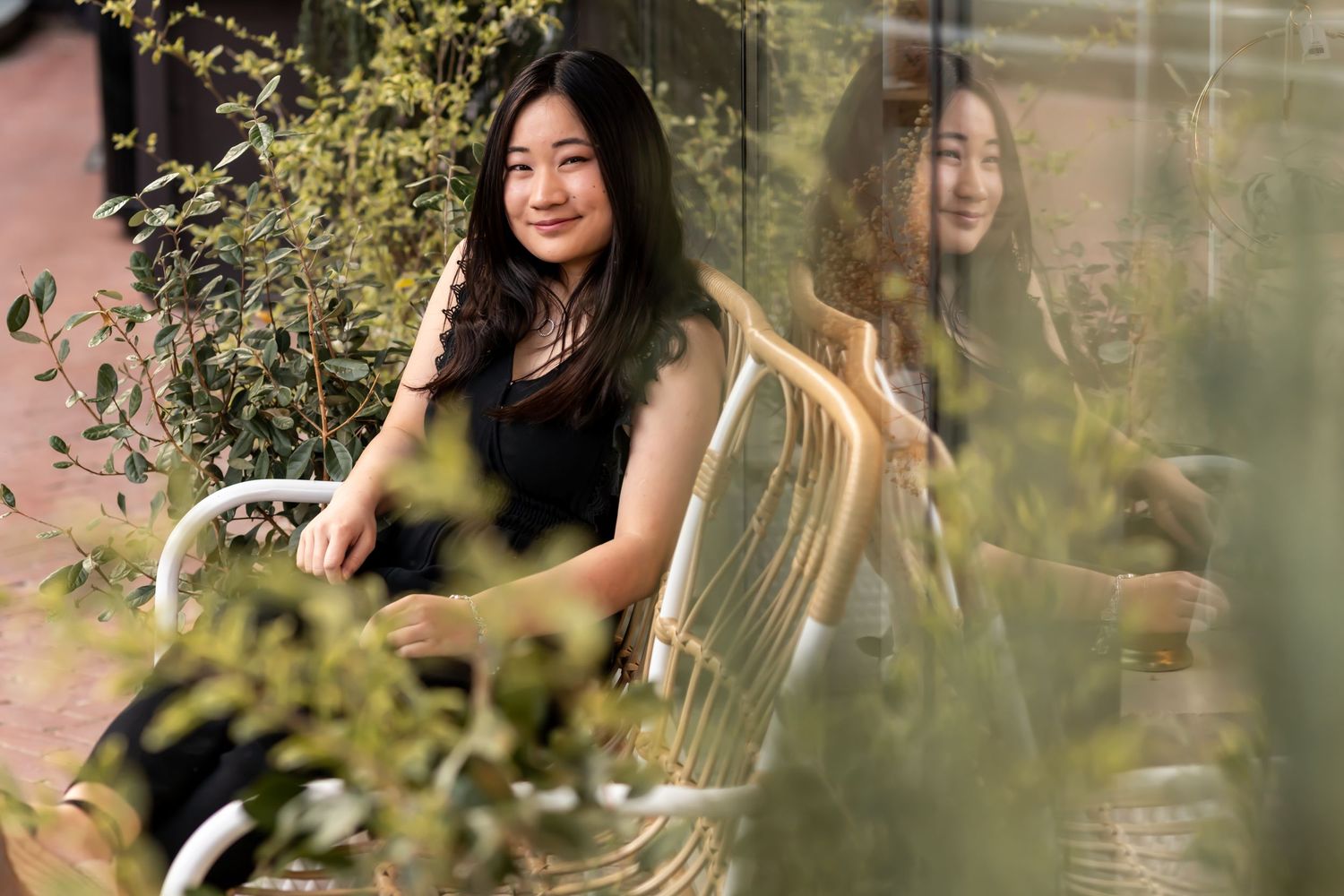 Artistic portrait through garden foliage with window reflection.