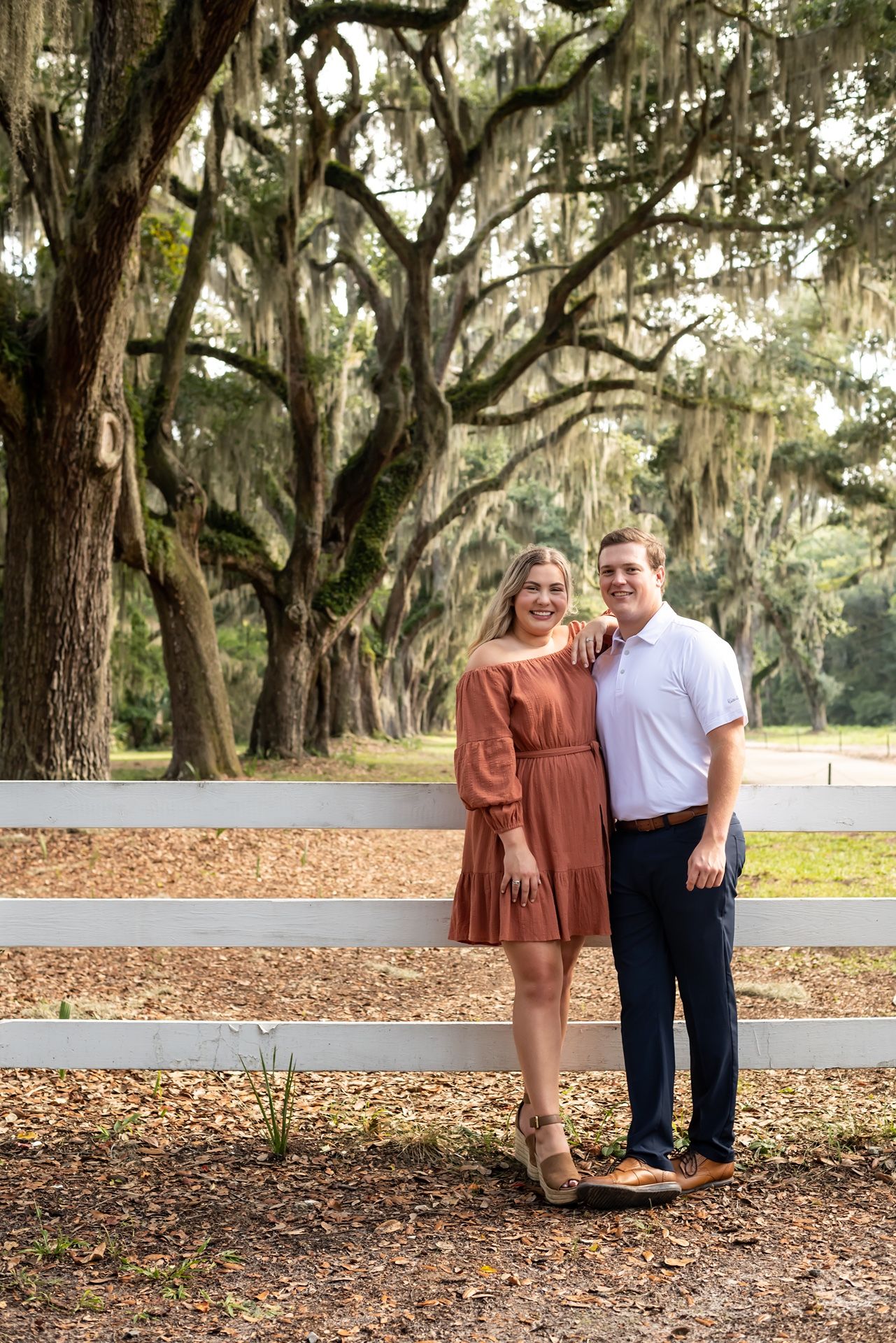 Couple poses under oak trees with hanging Spanish moss in a serene autumn setting.