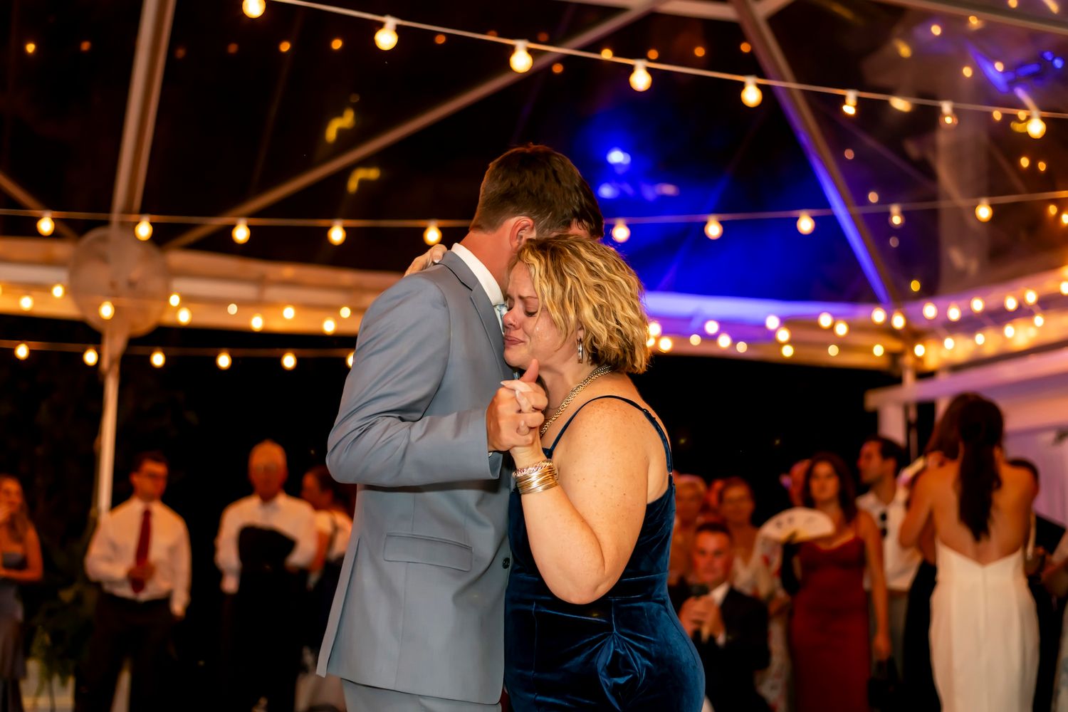 A couple shares an intimate dance moment under string lights at an evening wedding reception.