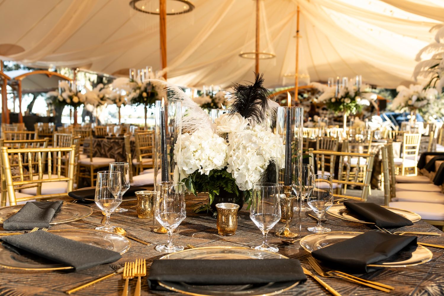 Elegant wedding reception tables decorated with white floral centerpieces and luxury table settings under draped fabric ceiling.