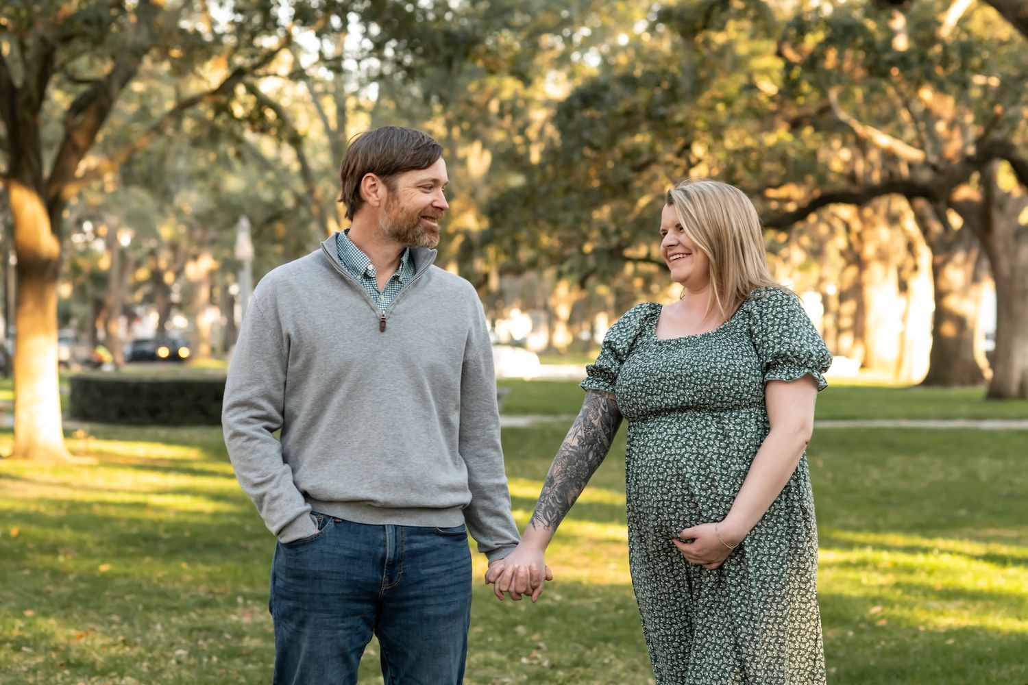 A couple shares a tender moment in a sunlit park while posing for fall engagement photos at golden hour.