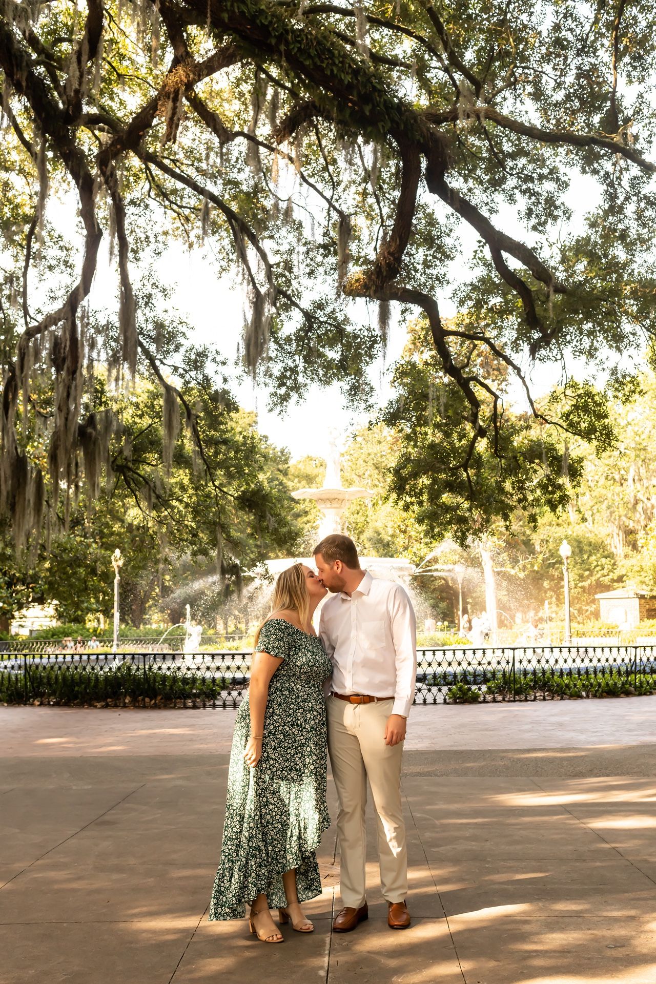 A couple shares a romantic moment under Spanish moss-draped trees in a sun-dappled courtyard garden.