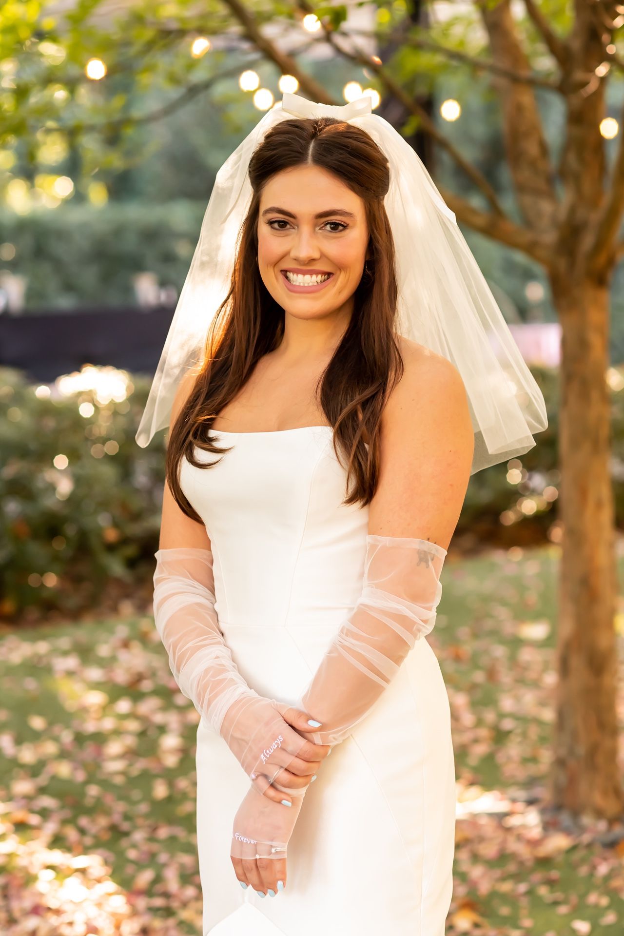 An elegant off-shoulder wedding dress with sheer sleeves is showcased in a romantic outdoor setting with bokeh lights.
