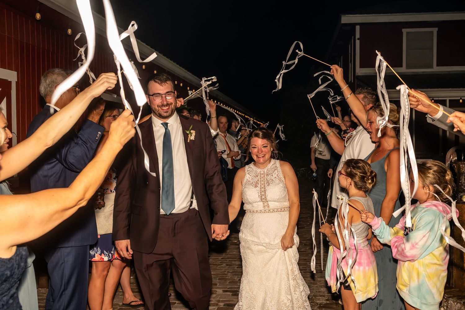 Newlyweds walk through an arch of guests holding sparklers during their evening wedding celebration exit.