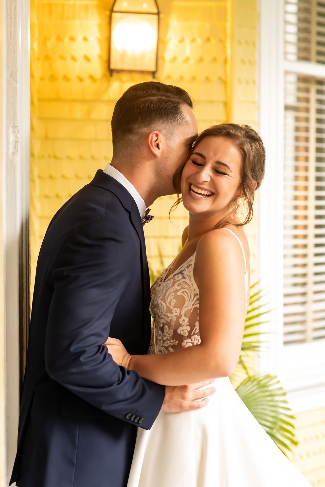 Sweet candid moment of a newly married couple sharing an intimate moment against a yellow wall with elegant lighting.