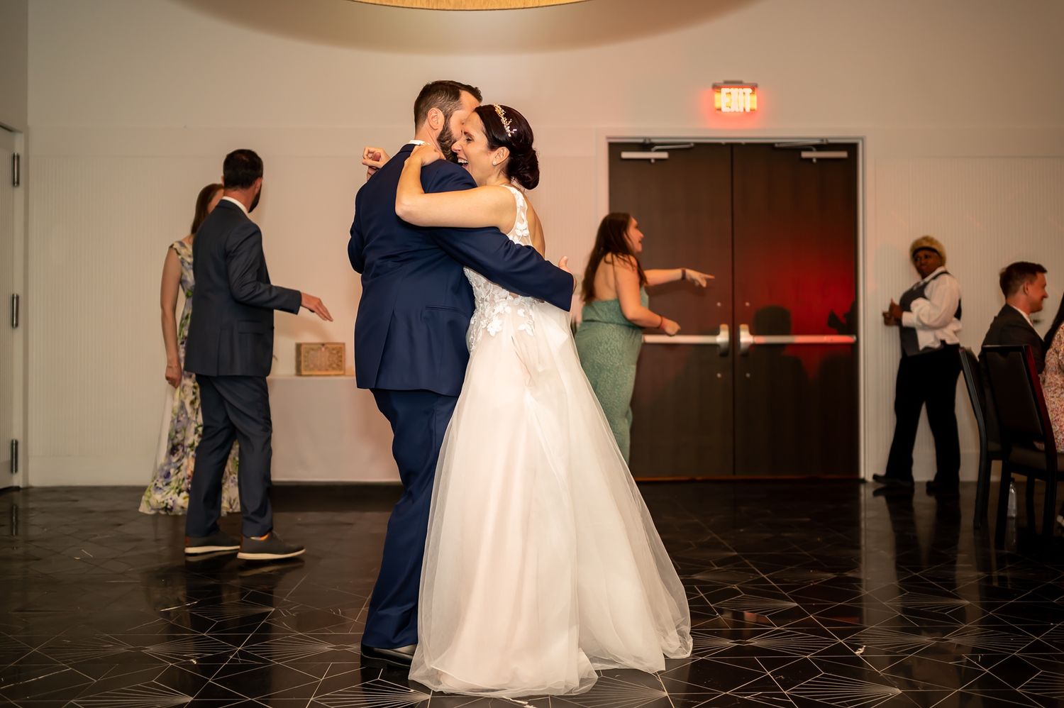 A couple in wedding attire shares a tender embrace on a dance floor while guests watch from the sidelines.