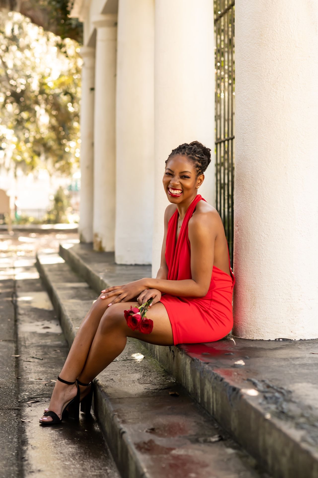 A photoshoot set showing a red dress against white colonial-style columns creating an elegant architectural backdrop.
