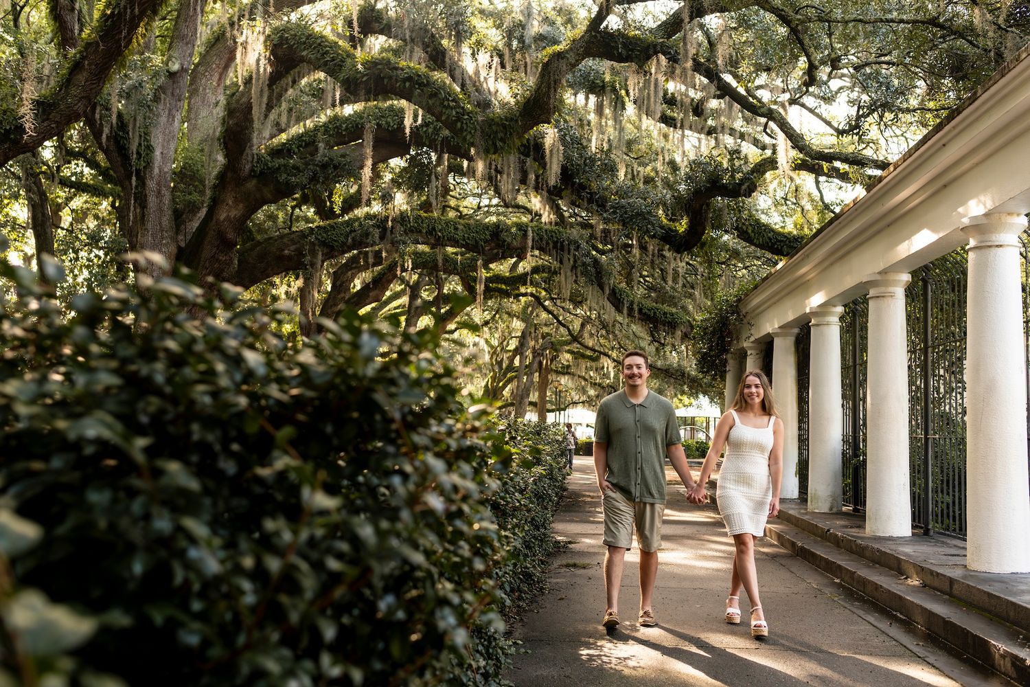Couple walking along a historic southern porch with Spanish moss draped oak trees overhead.