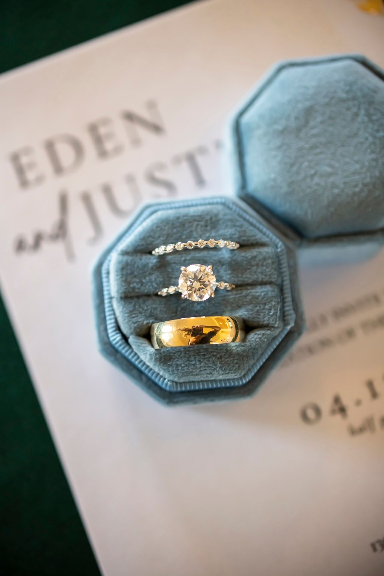 Wedding rings and engagement ring displayed in light blue velvet octagonal ring box with Eden and Just visible on paper.