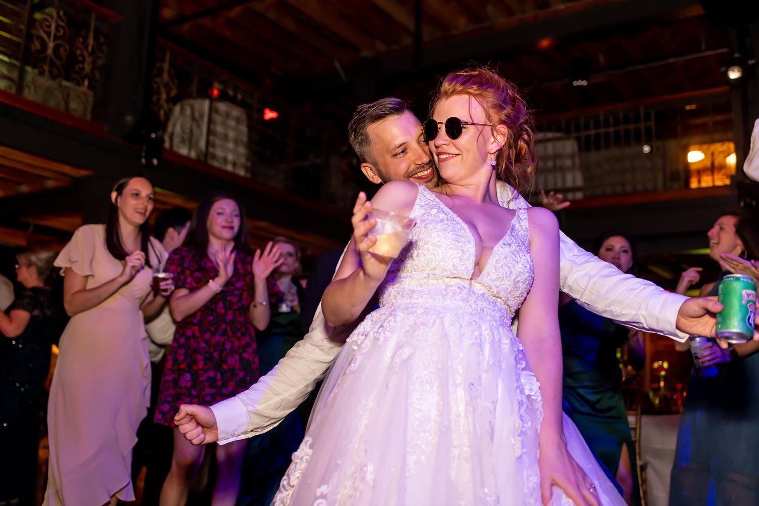 A couple dances together on a dimly lit dance floor with purple lighting and other people in the background.