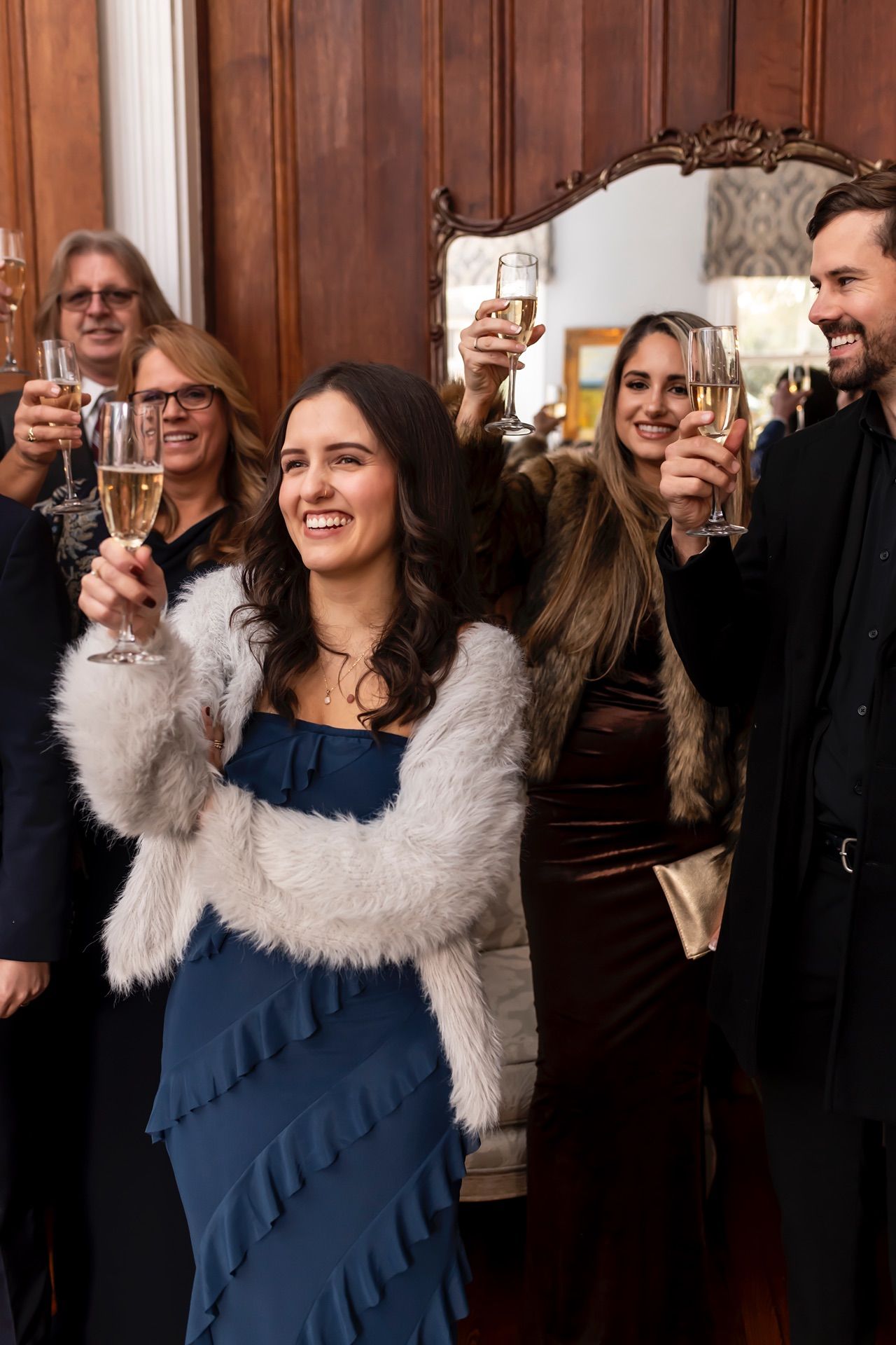 Group of friends raising champagne glasses in celebration at an elegant party with wood-paneled walls.