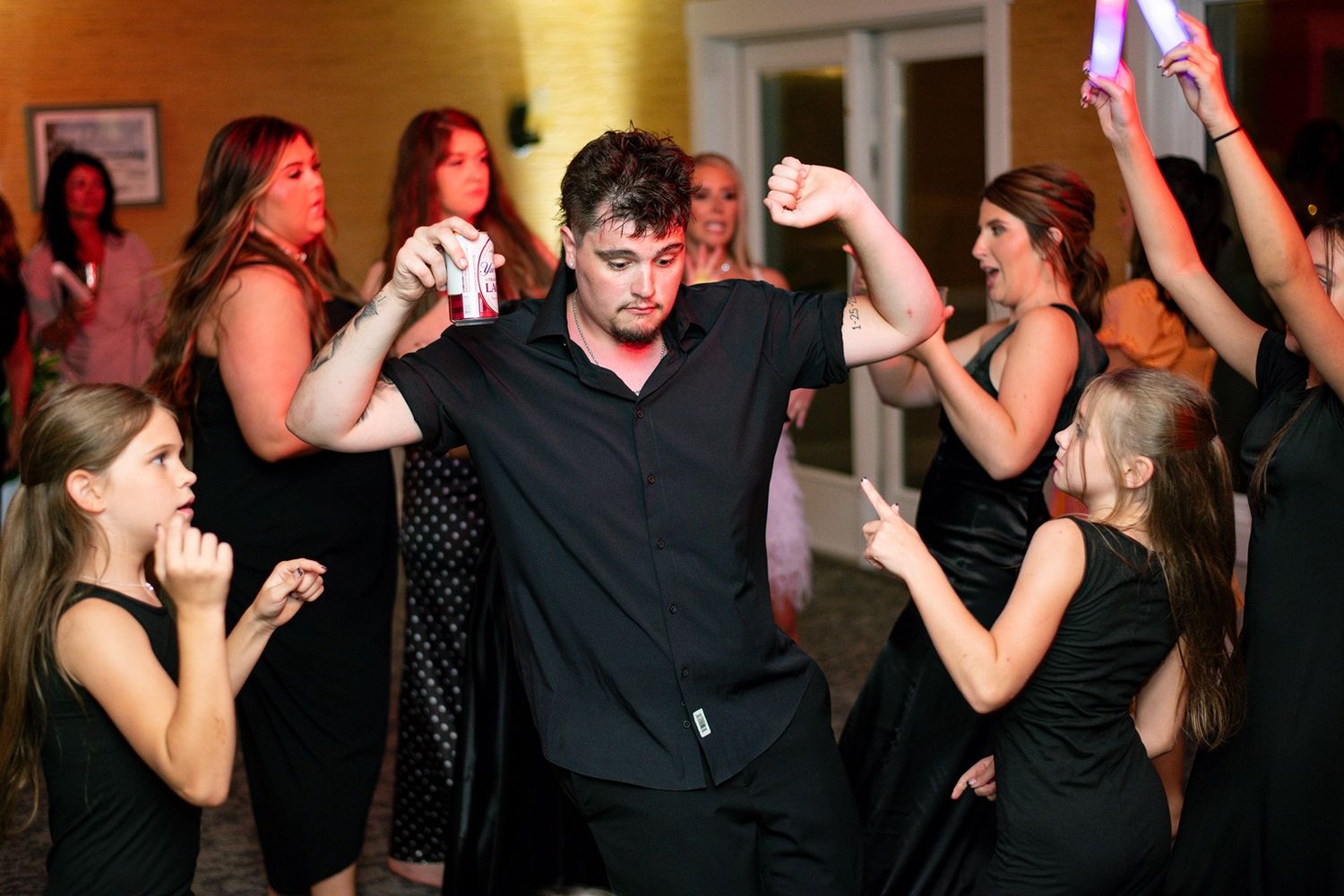 Energetic dancing at a party with guests holding glow sticks in a dimly lit room.
