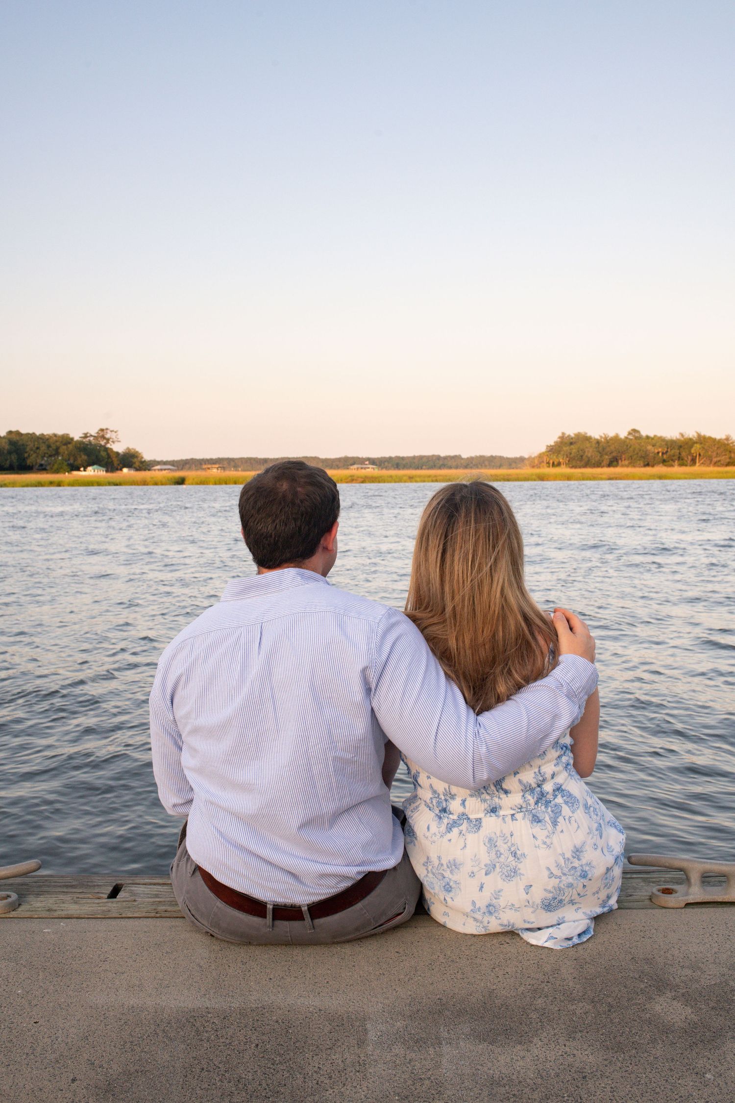 Two people sitting together on a dock watching a peaceful sunset over a calm lake.