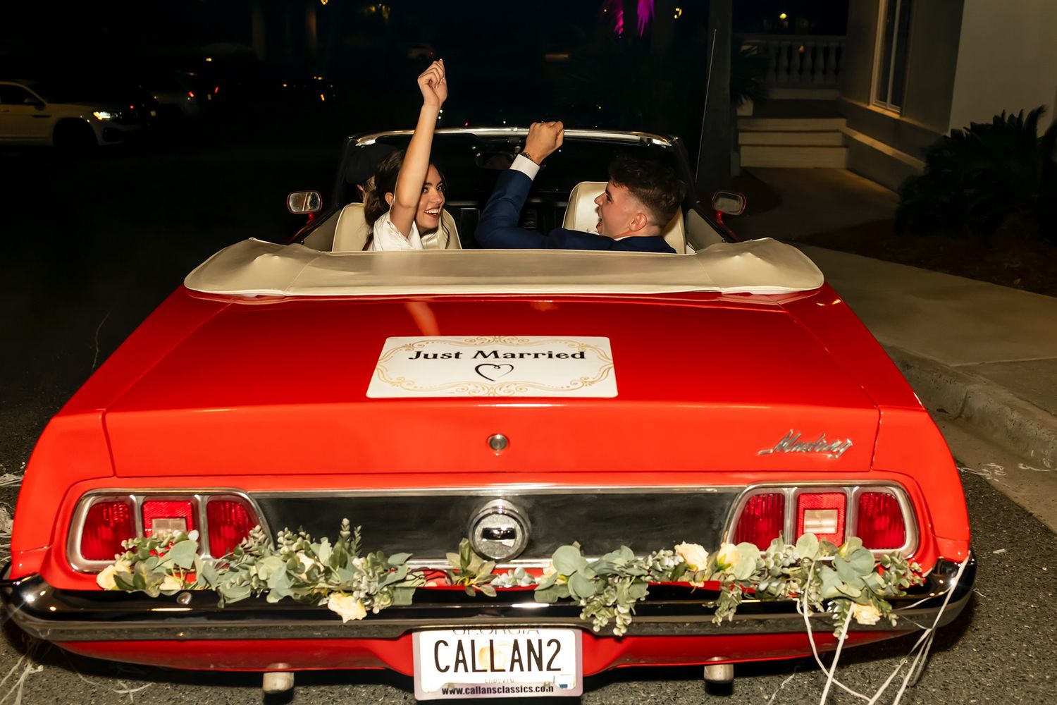 A classic bright red Ford Mustang convertible decorated with 'Just Married' signage parked at night.