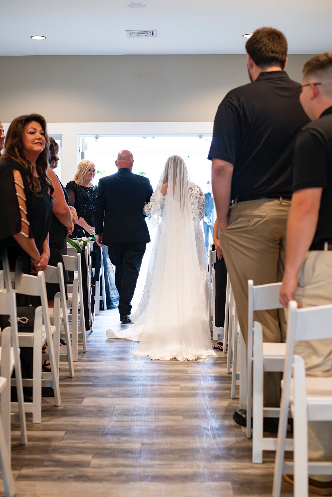 A wedding ceremony setup with white chairs and a bride in a flowing white gown standing at the end of the aisle.